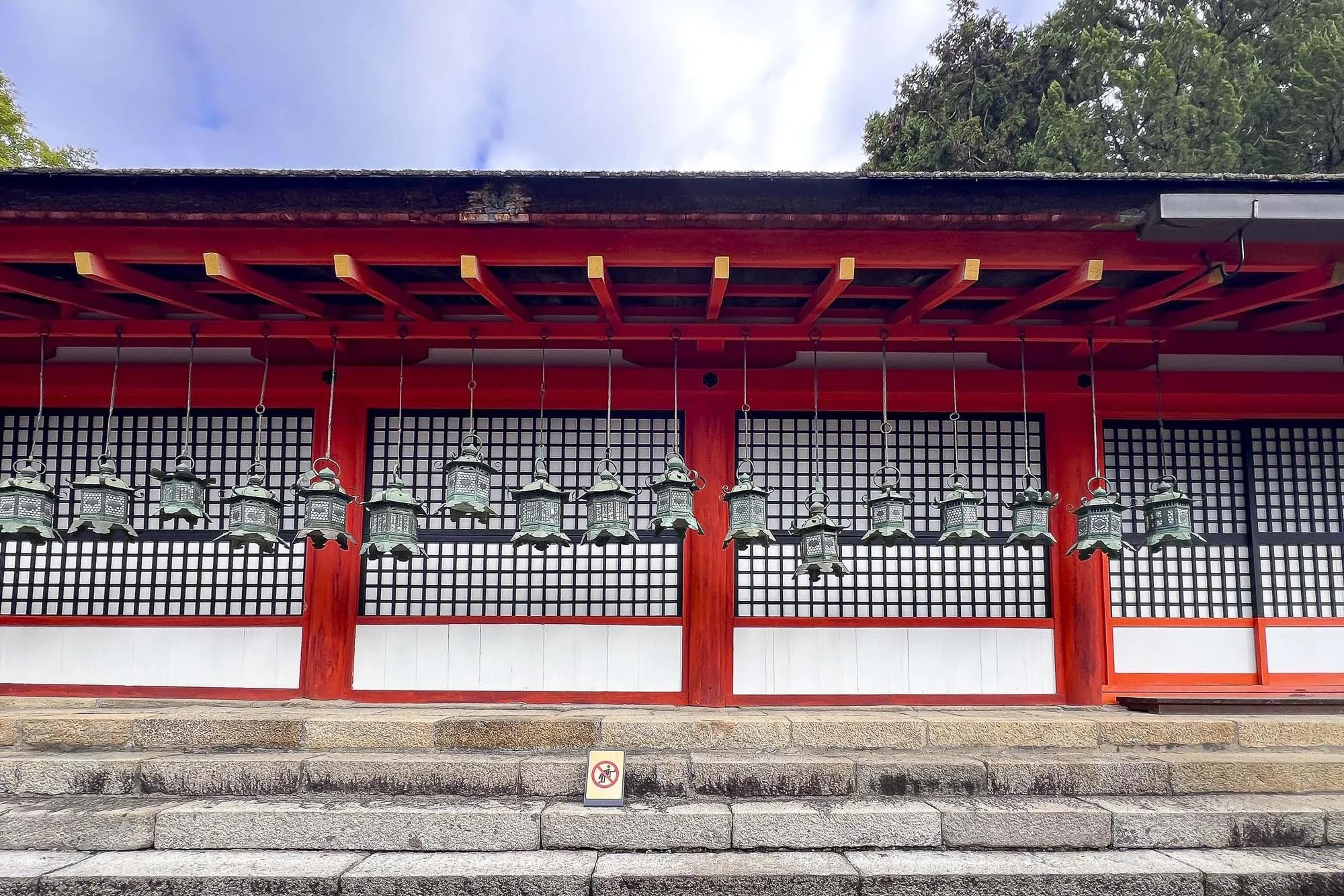 Traditional Japanese temple building with red wooden framework and multiple hanging lanterns, stone steps in front, and a no smoking sign.
