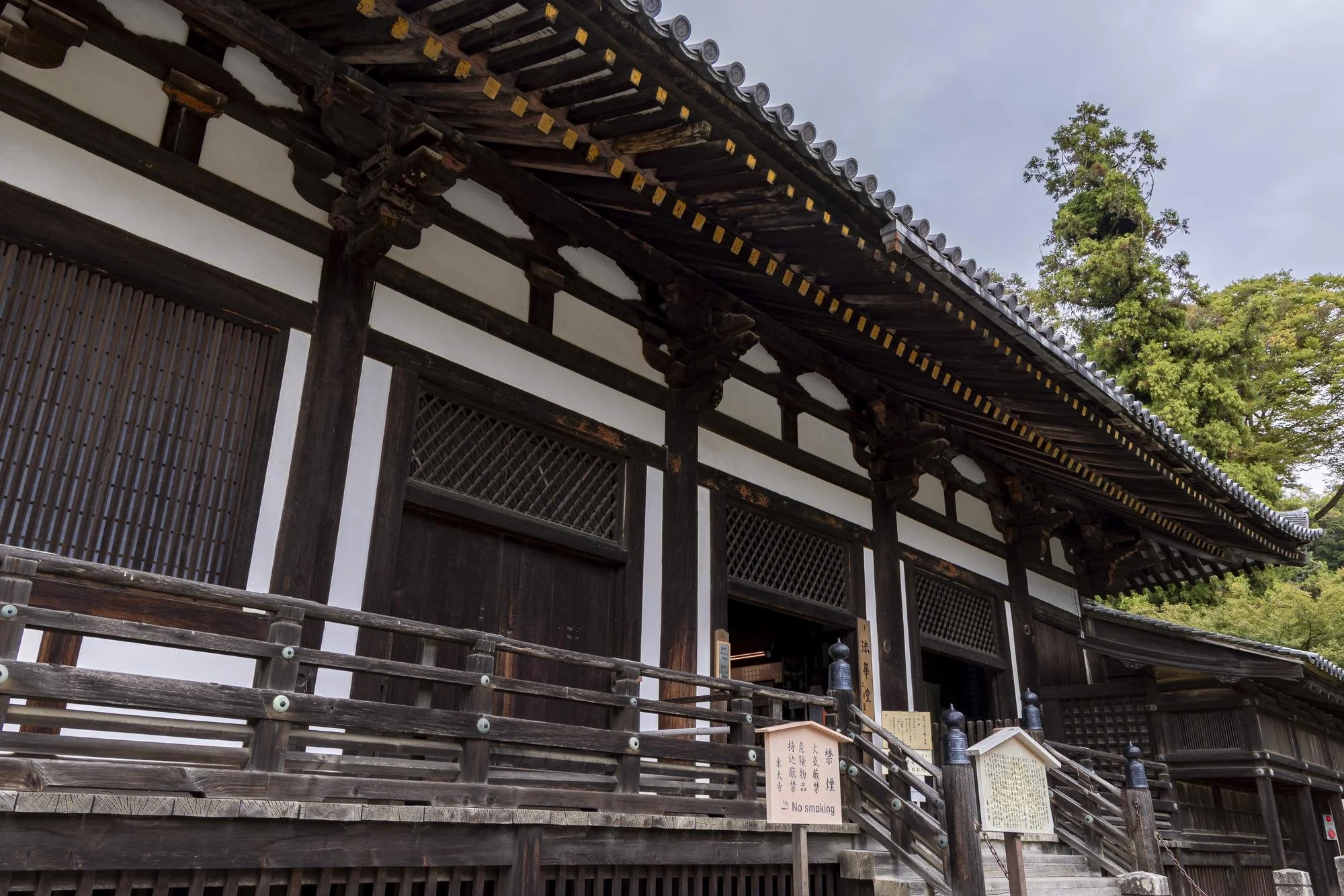 Traditional Japanese wooden temple or building with detailed roof and lattice windows, surrounded by green trees.