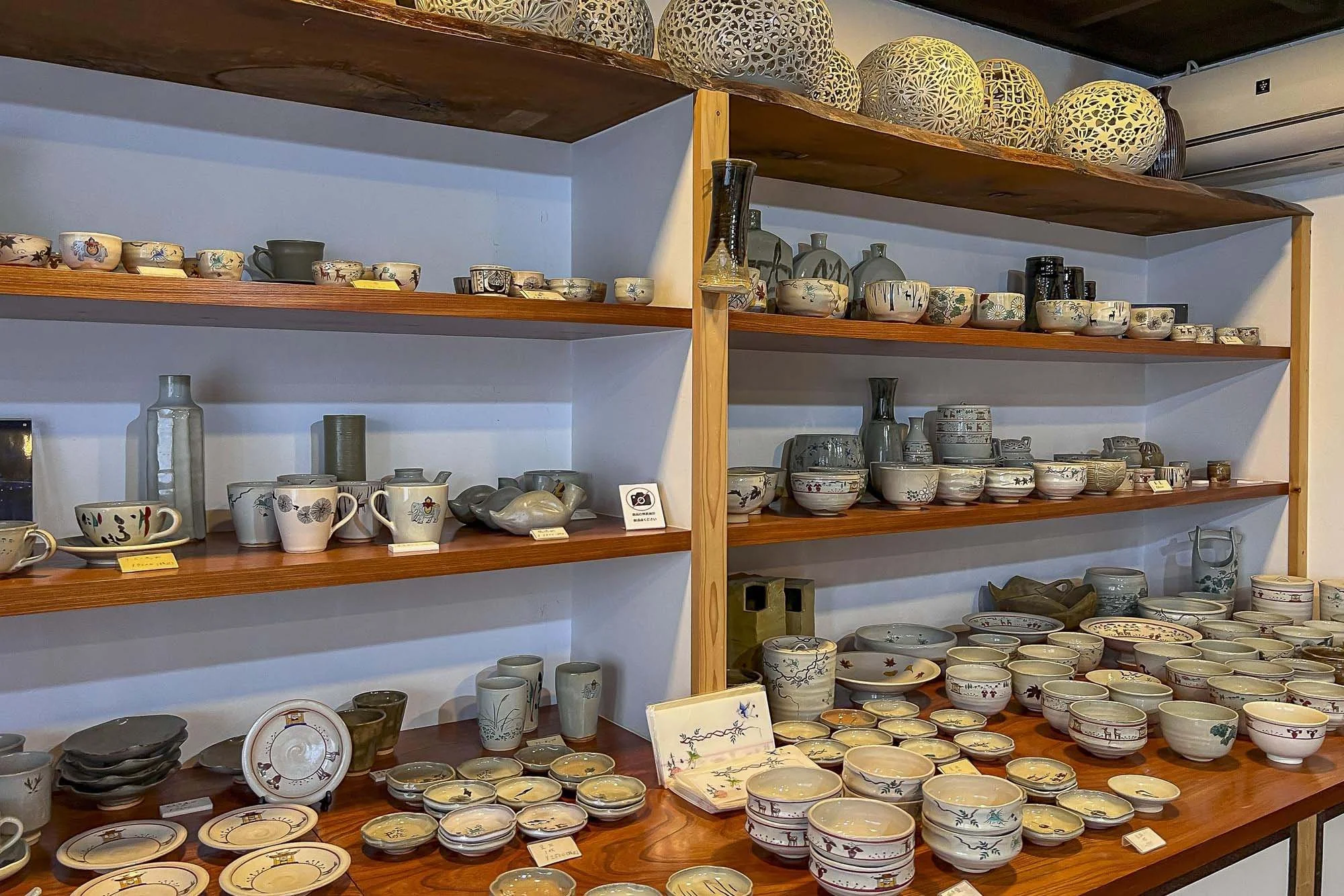Wooden shelves displaying a variety of ceramic bowls, plates, and vases, with some decorative or patterned items on top.