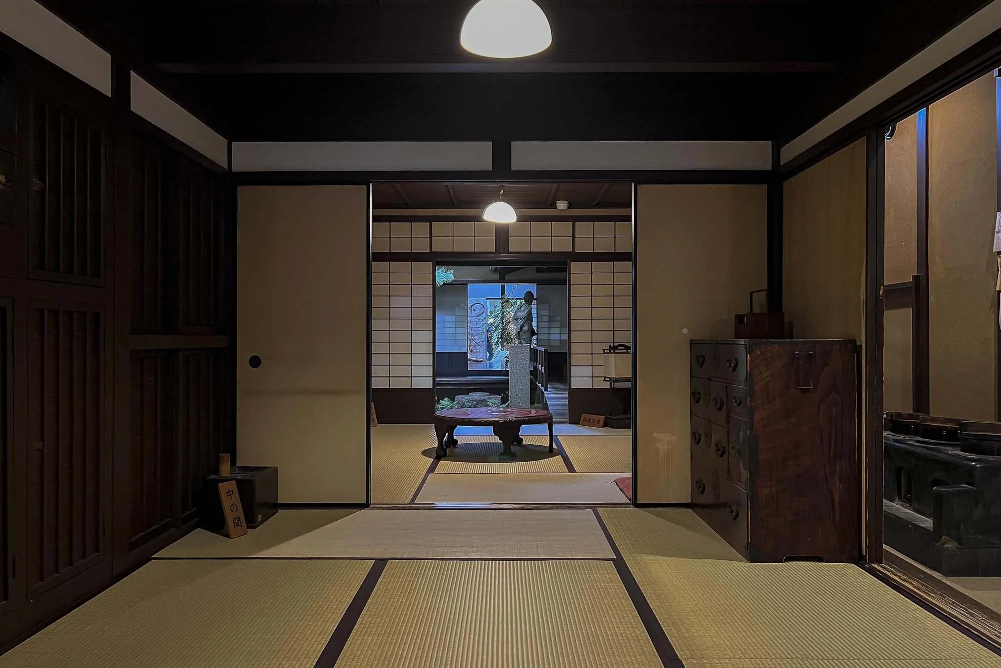 Interior of a traditional Japanese room with tatami mats, sliding doors, and a person standing near a window.