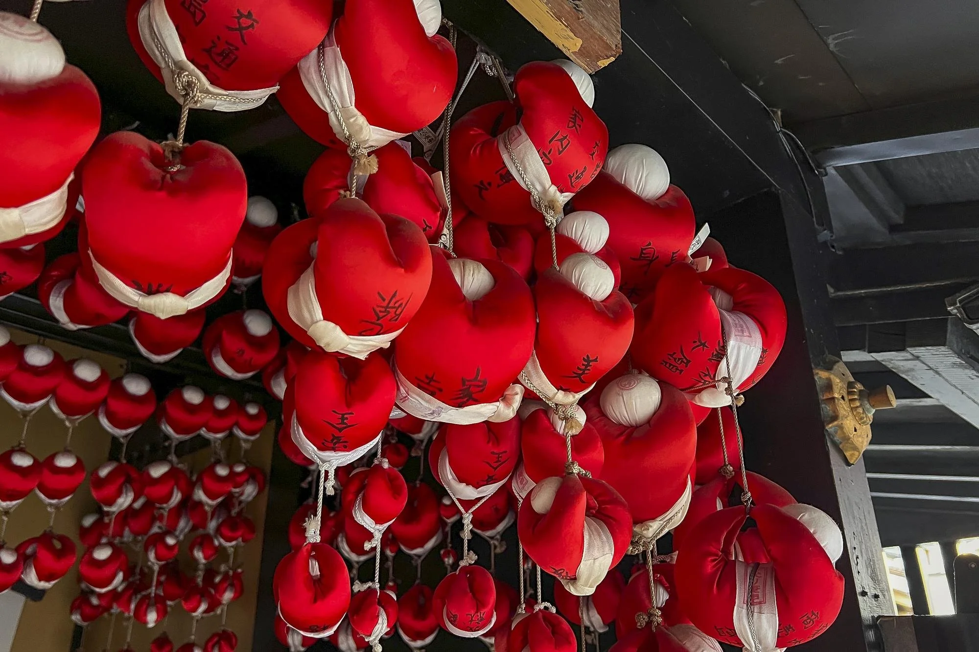 Numerous red fabric pouches with white bands and black Chinese characters hanging from strings, typically used as prayer or fortune charms in Asian culture.
