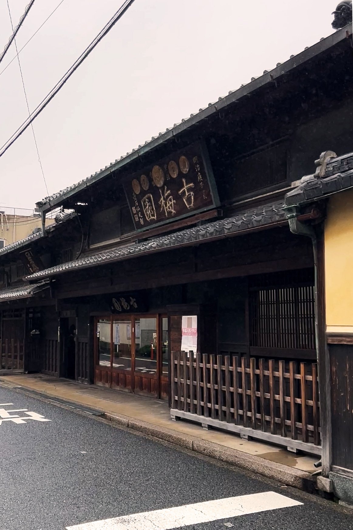 Traditional Japanese building with dark wooden exterior, tiled roof, and a signboard with Japanese characters.