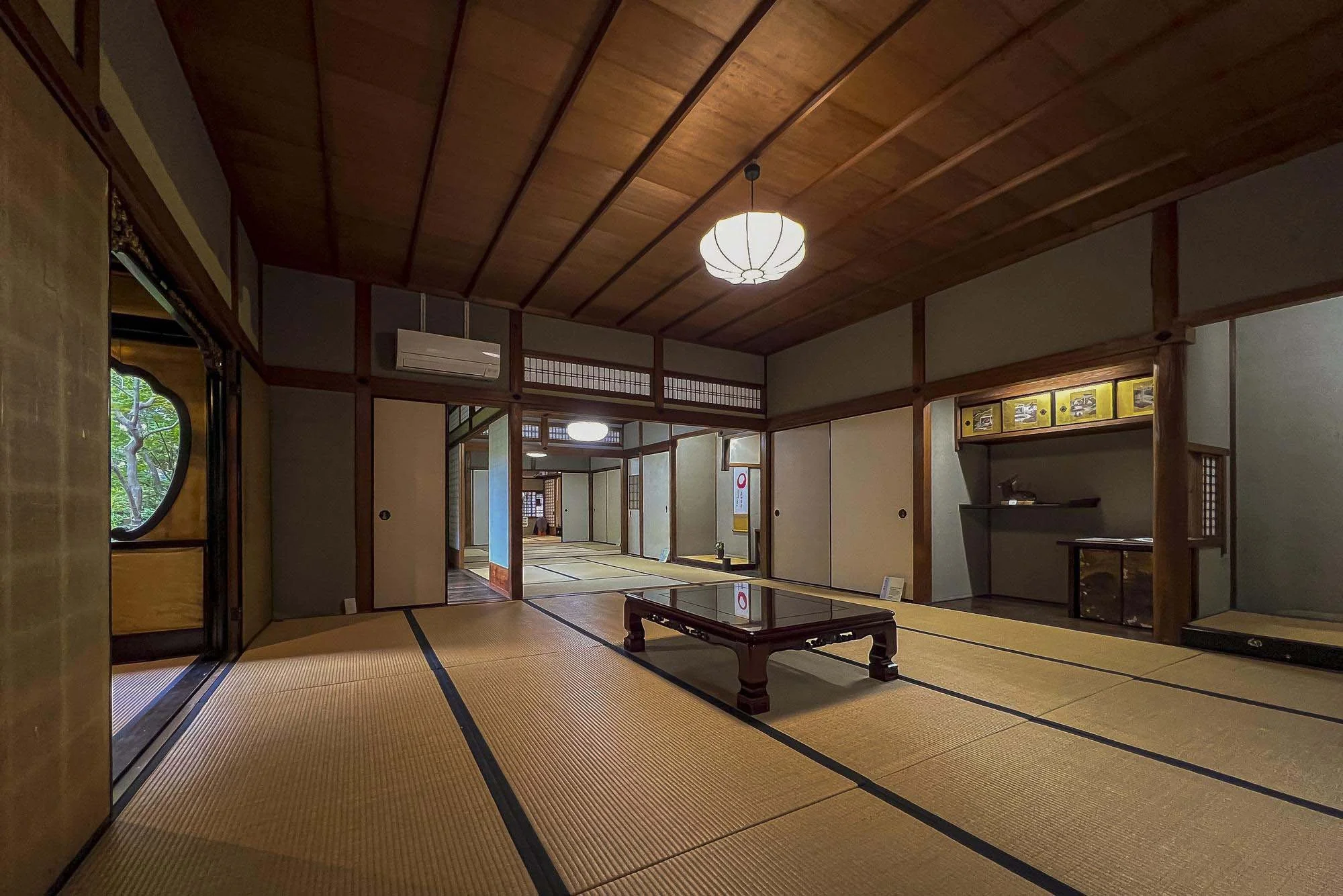 Naramachi: Traditional Japanese room with tatami mats, sliding doors, wooden ceiling, and minimal furnishings including a low wooden table and display shelves.
