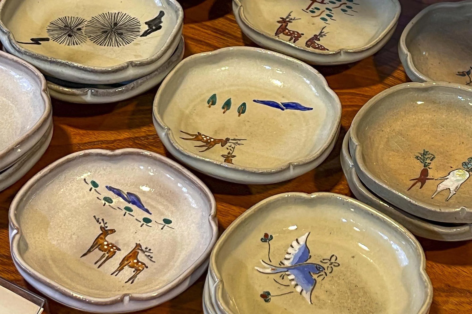 Decorative ceramic bowls with painted wildlife scenes, including deer, birds, and insects, arranged on a wooden surface.