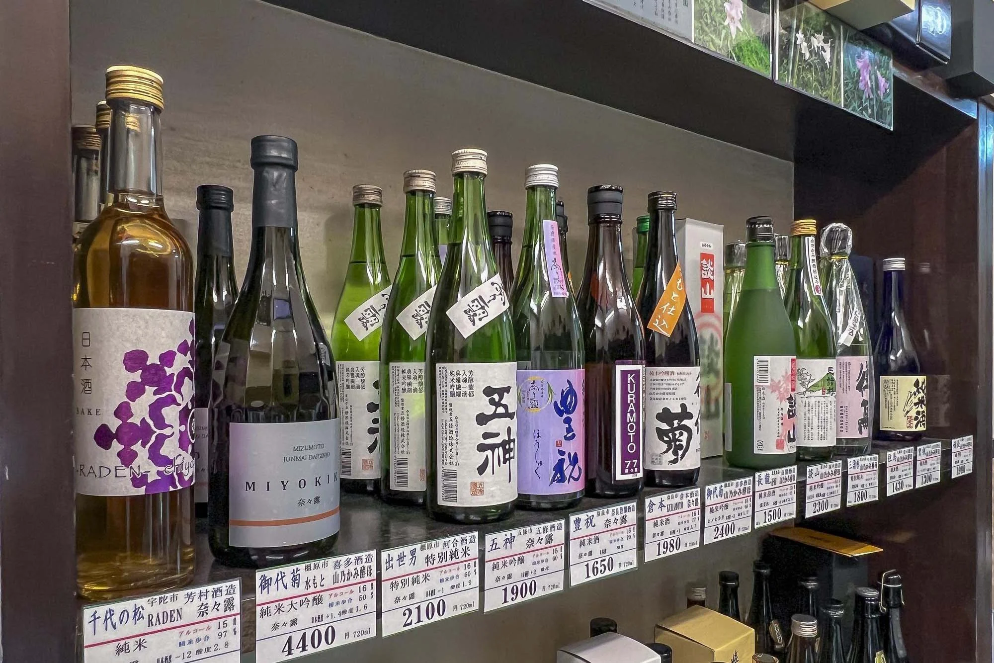 A shelf of various bottles of sake, each with different labels and prices, displayed in a store.