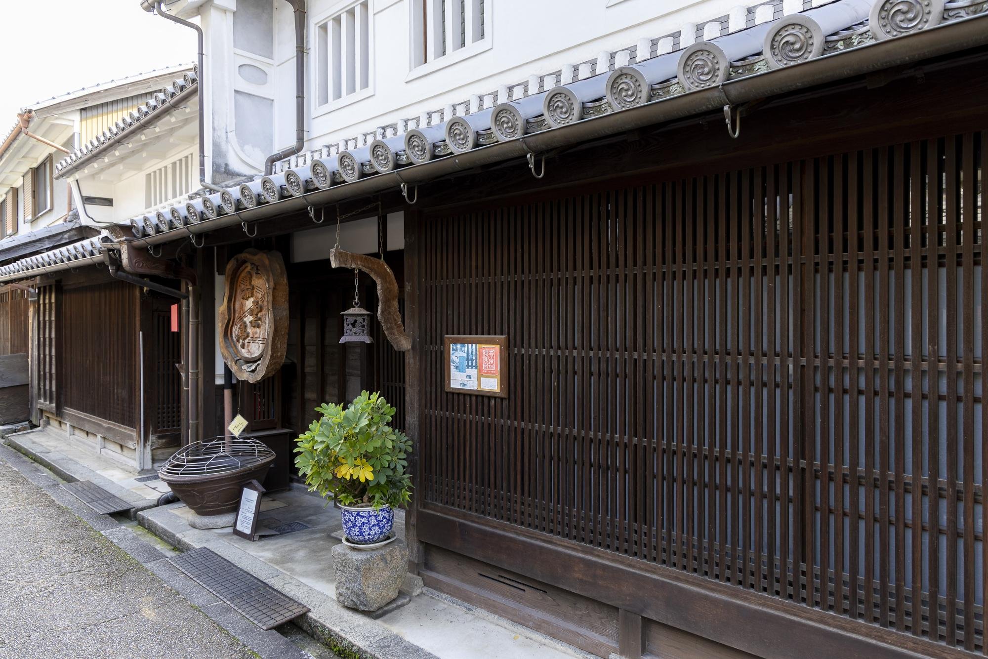 Traditional Japanese building with wooden sliding doors, decorative elements, and a potted plant outside.