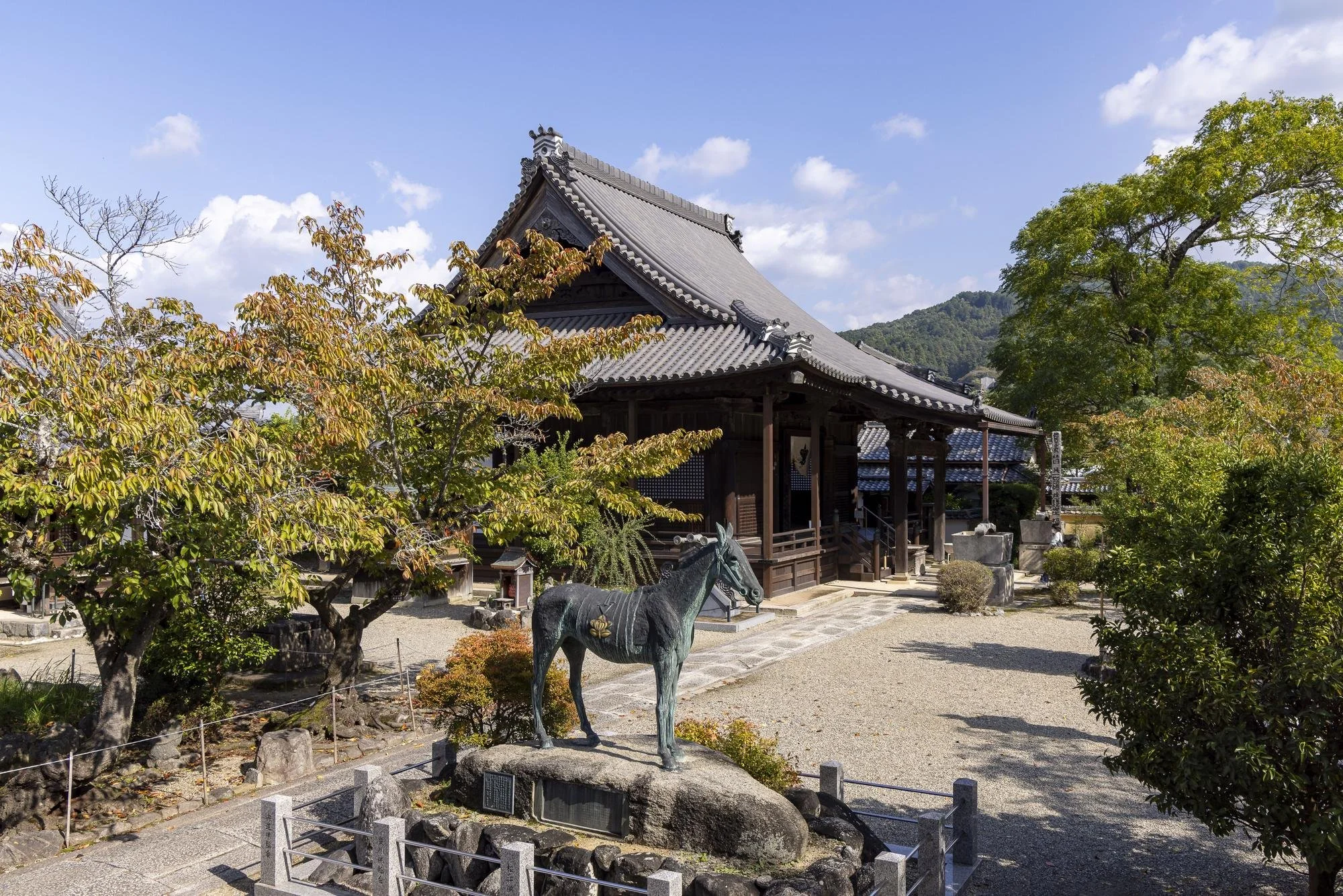 Traditional Japanese shrine with wooden architecture, stone lanterns, and greenery in a peaceful outdoor setting under a partly cloudy sky.