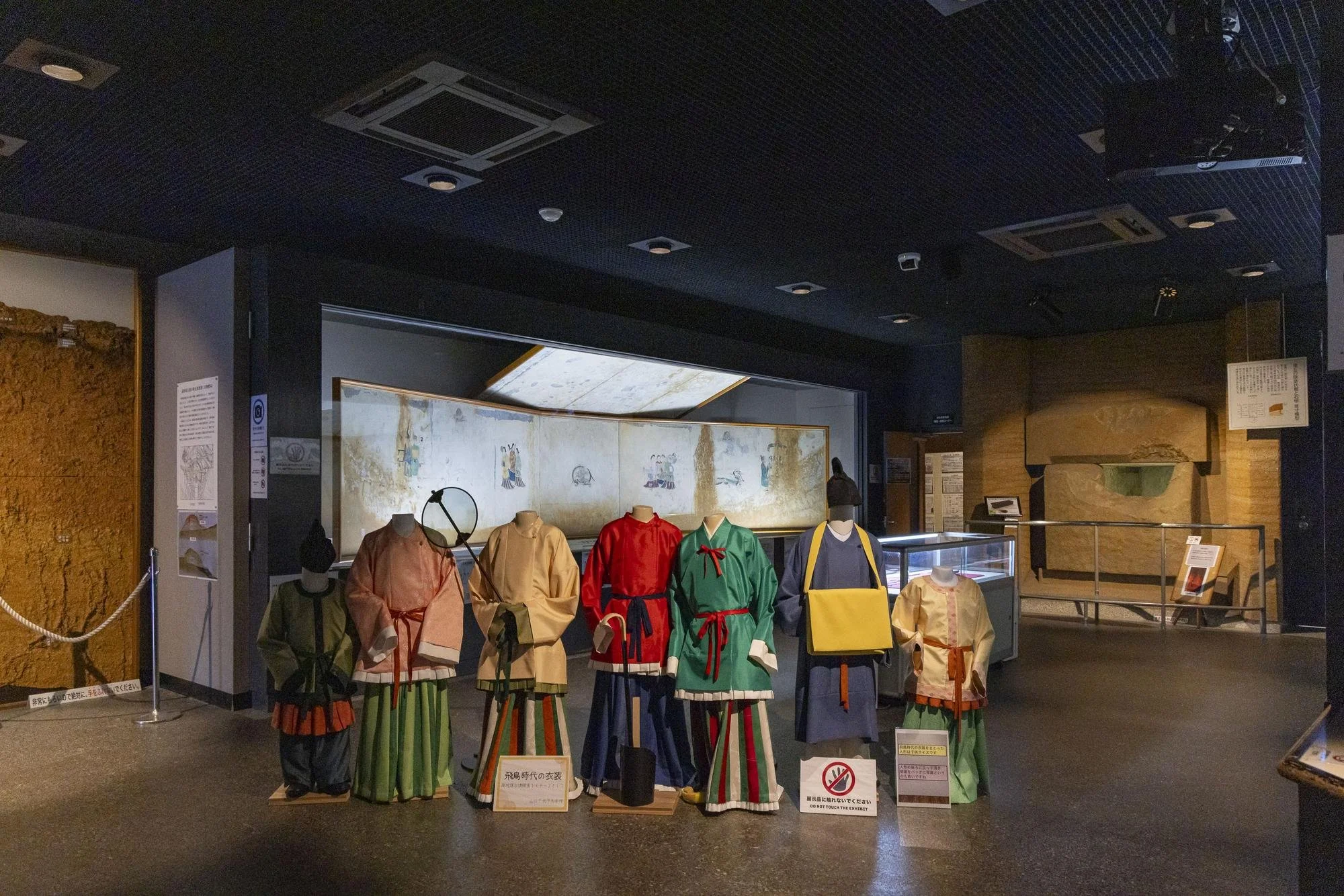 Display of traditional Japanese clothing on mannequins inside a museum, with a backdrop of historical paintings and information signs.