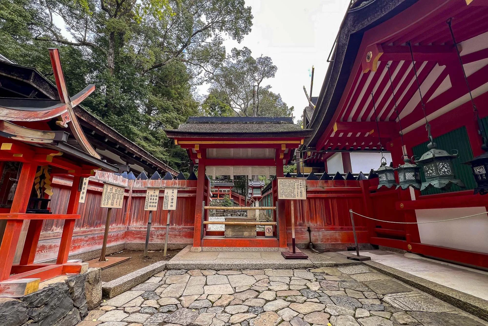 Traditional Japanese shrine with red wooden structures and stone pathway, surrounded by trees.