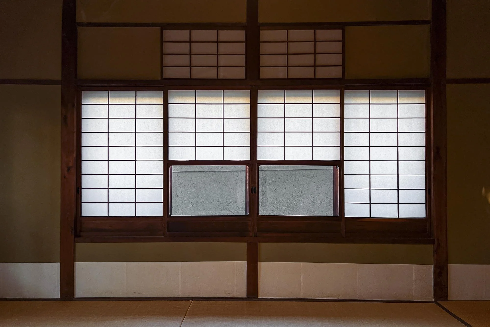 Traditional Japanese shoji window with wooden frame and translucent paper panels in a room with tatami mats.