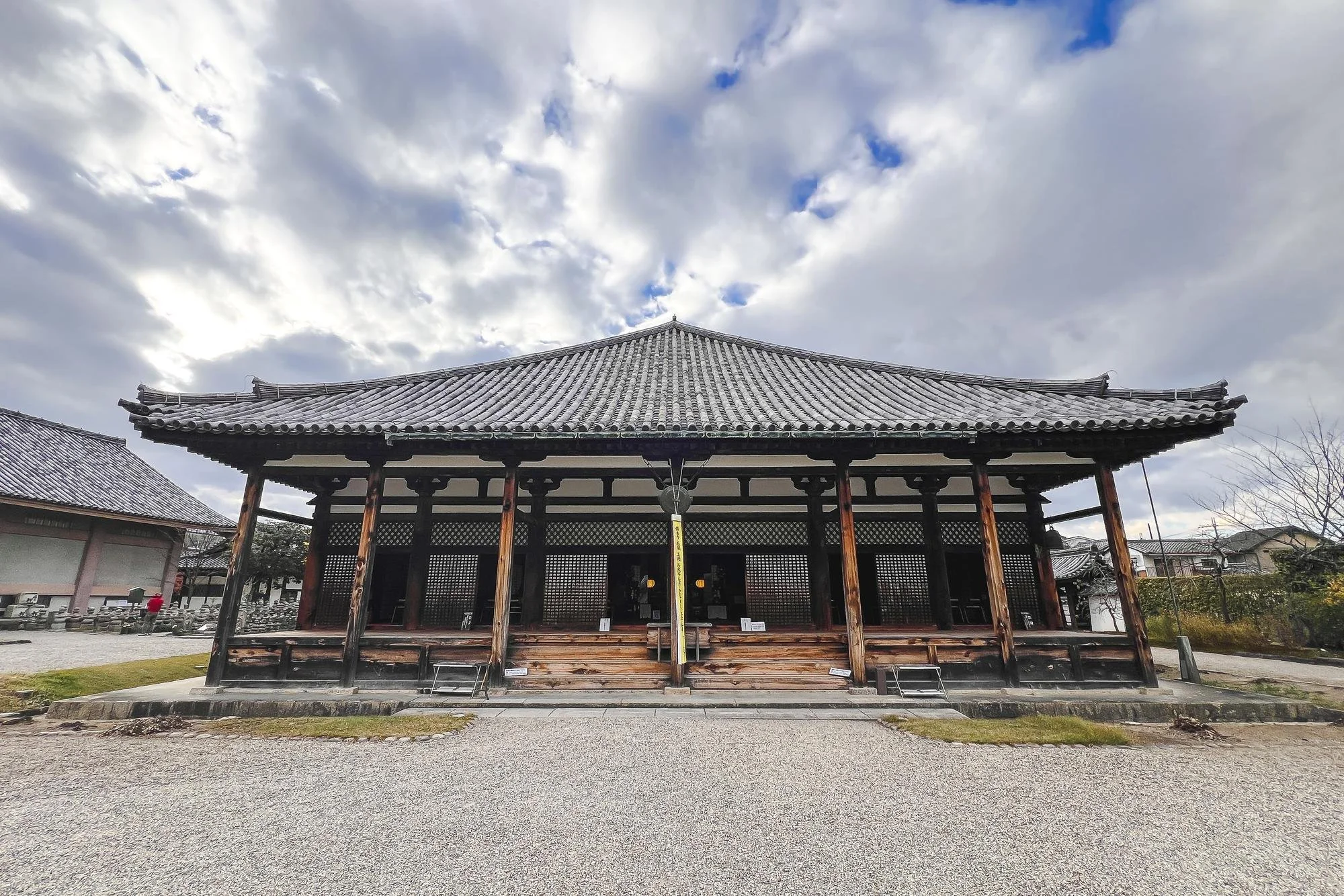 Traditional Japanese wooden temple amid cloudy sky, with gravel ground in front.