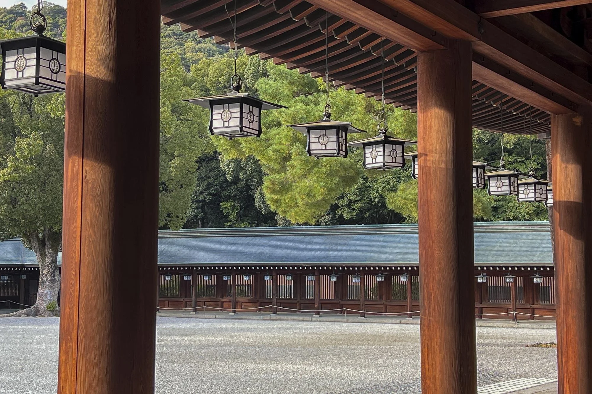 Traditional Japanese temple with hanging lanterns and wooden pillars, surrounded by green trees.