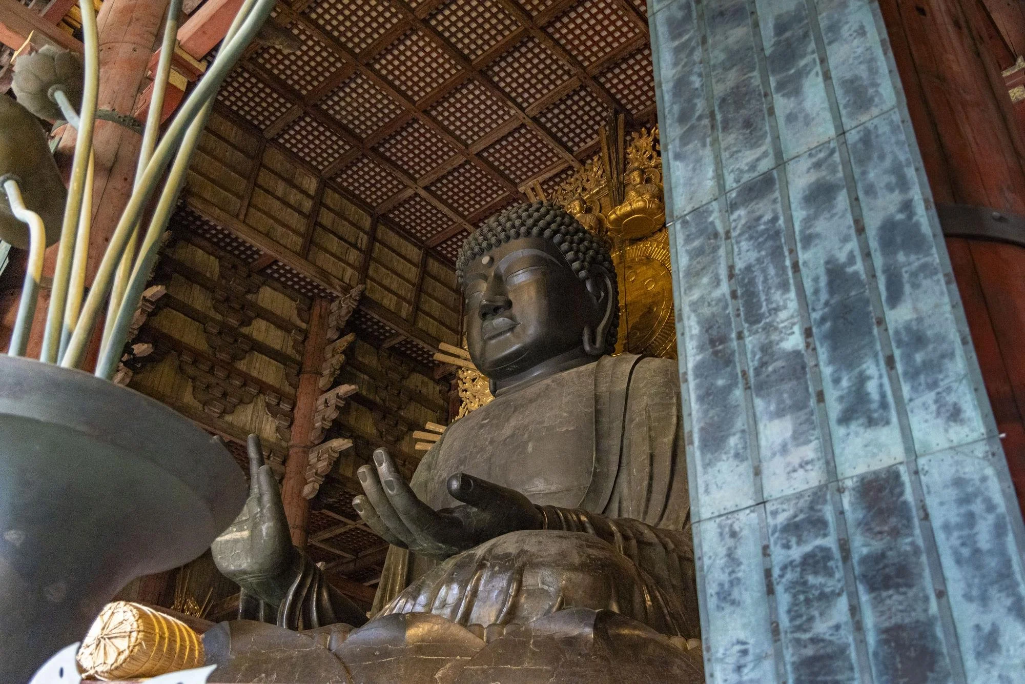 A large seated bronze Buddha statue inside a wooden temple, with intricate woodwork on the ceiling and gold accents behind the statue.