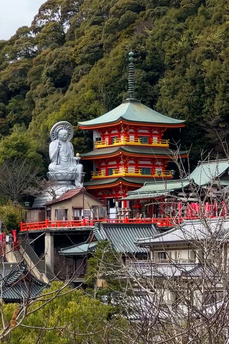 Chogosonshi-ji Temple: A Japanese temple complex nestled among trees, featuring a three-tier pagoda, a large silver Buddha statue, and traditional buildings with tiled roofs.