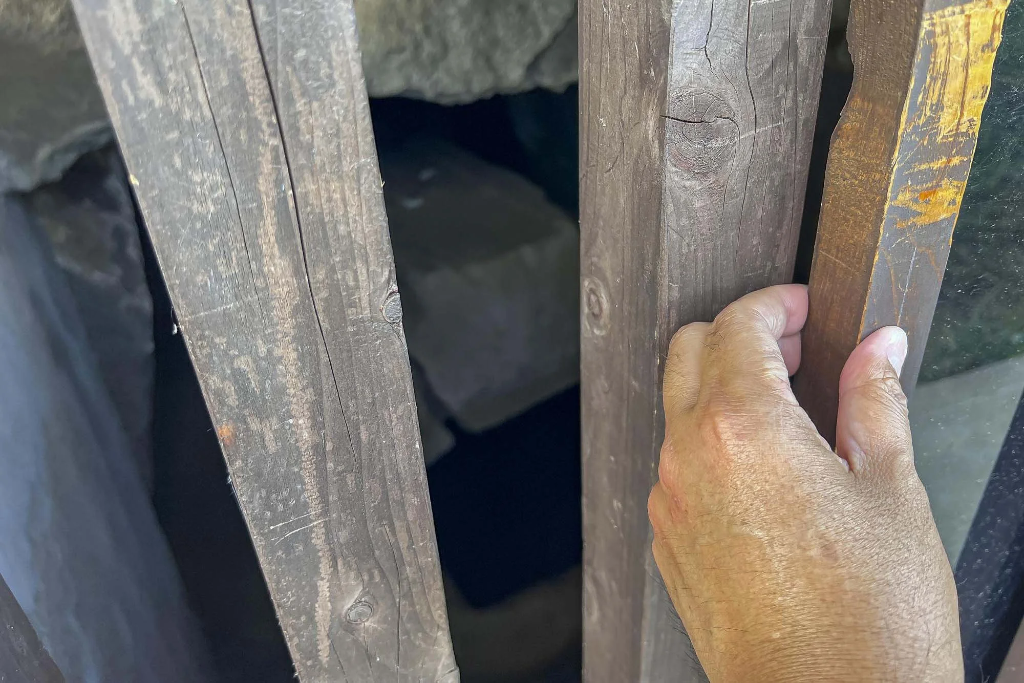 A hand pulling open wooden gate or door, revealing a dark background.