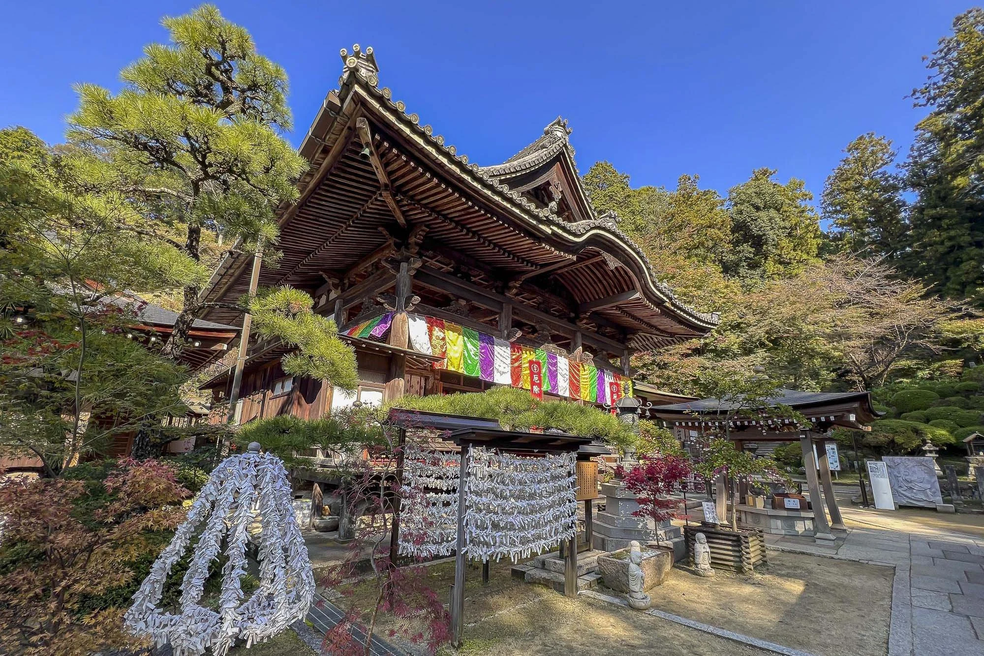 Traditional Japanese temple with colorful banners, surrounded by visitors, under a clear blue sky.