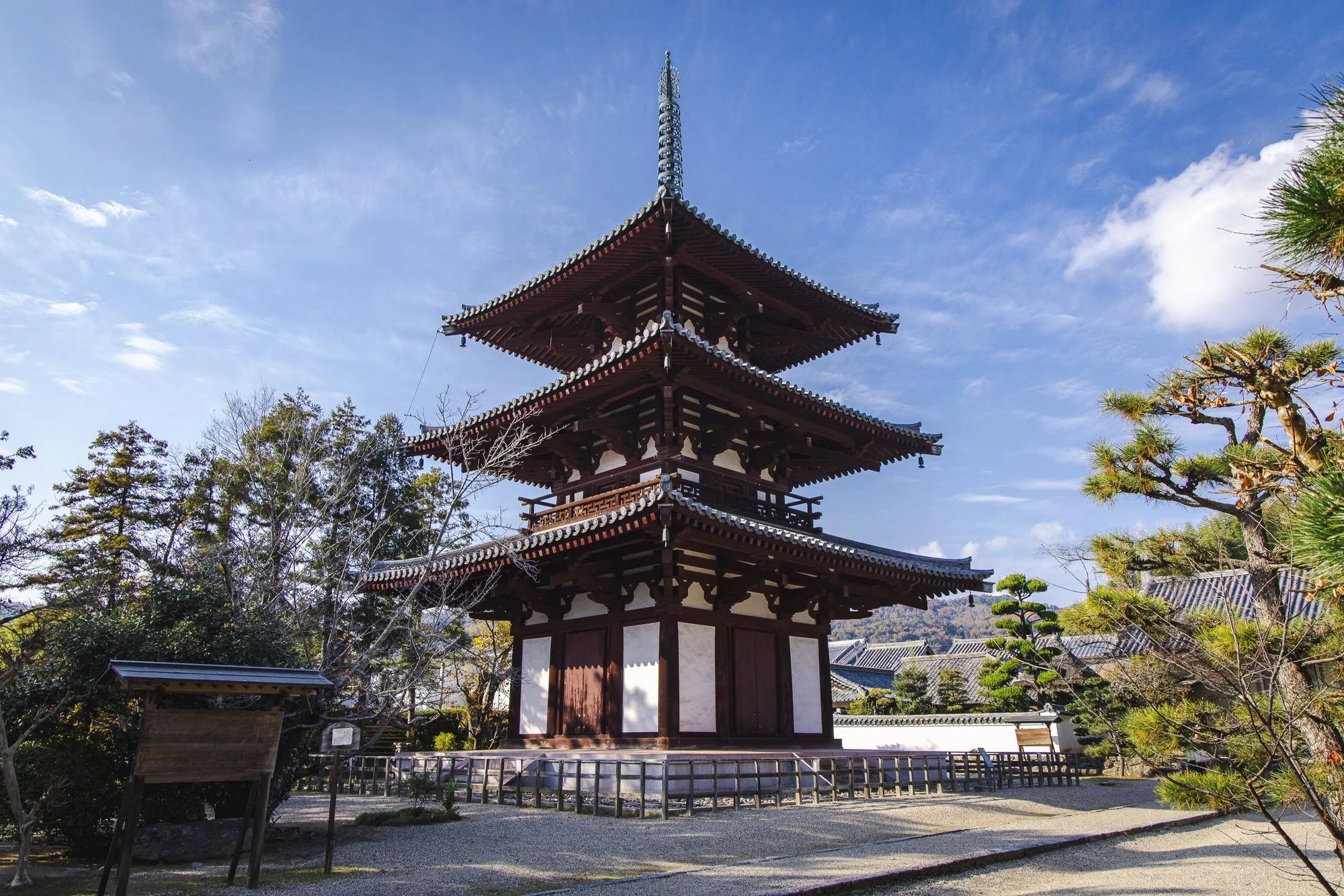 Traditional Japanese three-tiered pagoda with wooden architecture, surrounded by trees and a clear blue sky.
