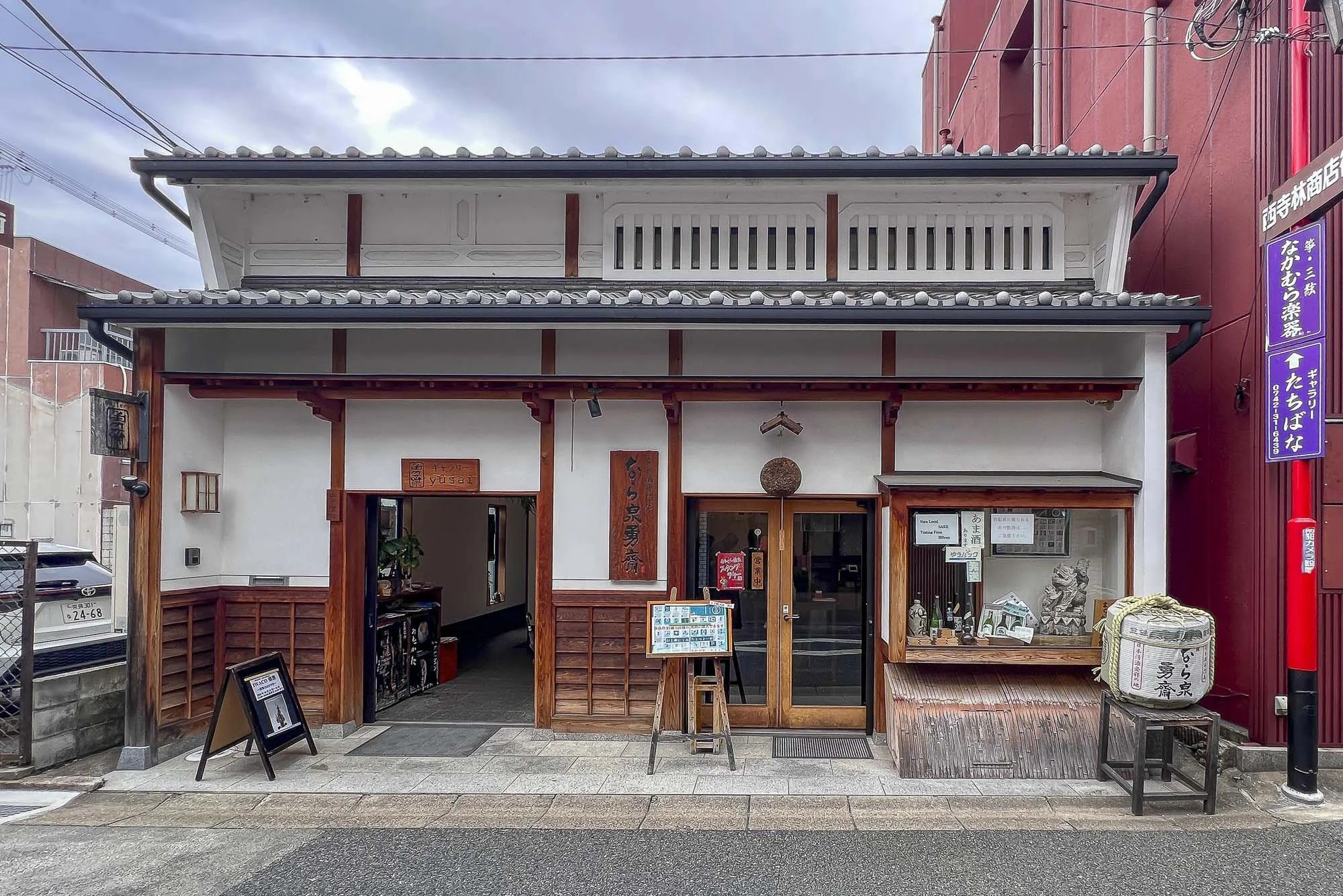 Nara Izumi Yusai: Traditional Japanese liquor store, storefront with wooden framing and white walls, featuring a hanging spherical ornament, a display window with a dragon sculpture, and signs in Japanese.