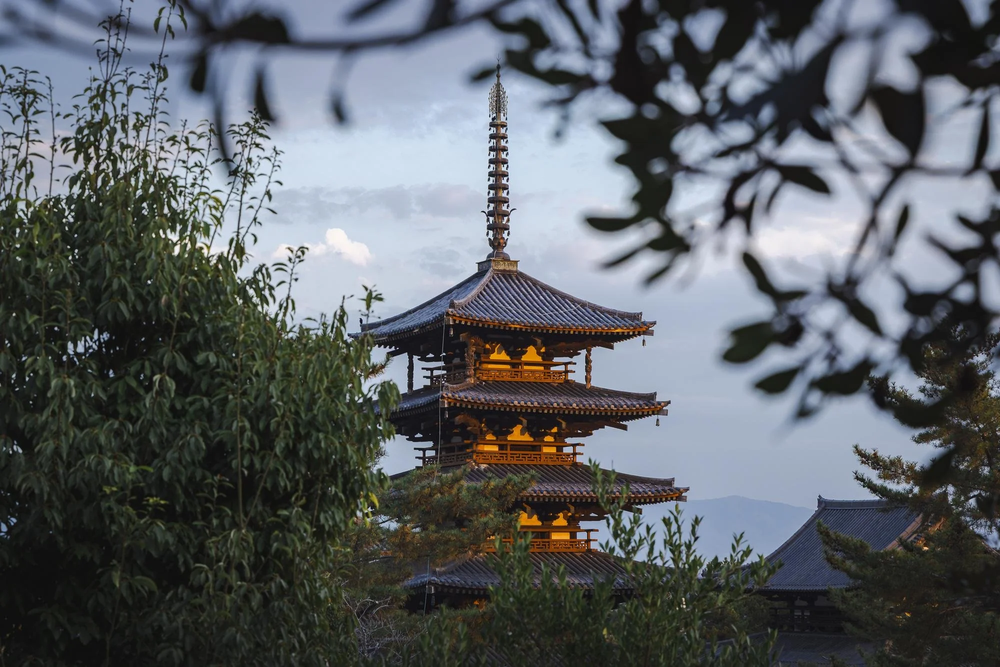 Traditional Japanese pagoda surrounded by lush trees with a clear sky in the background.