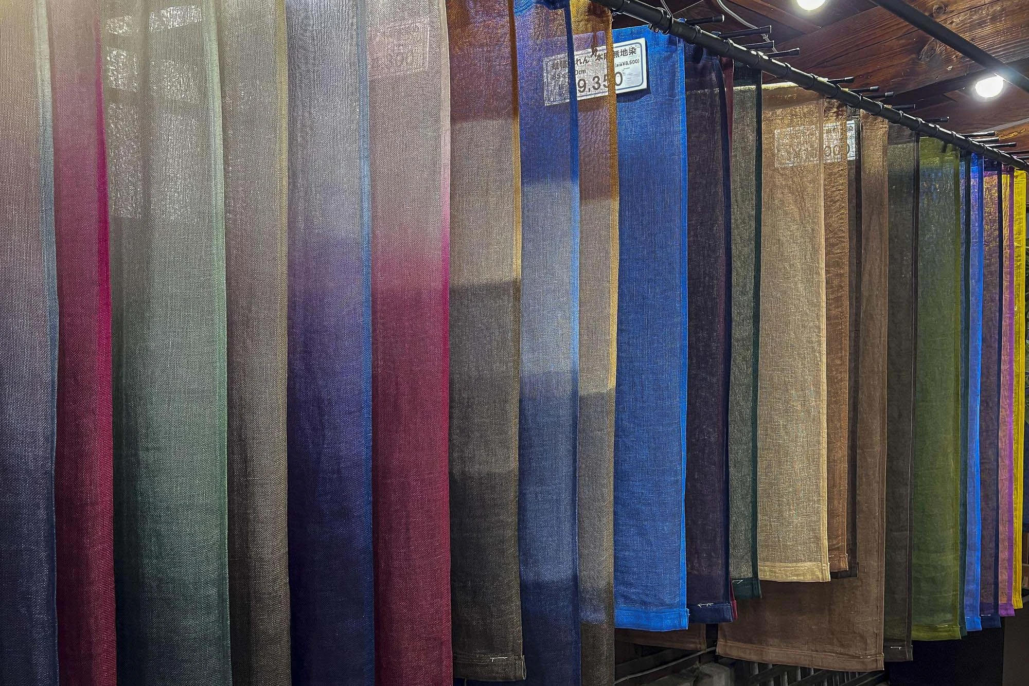 Rows of colorful fabric samples hanging on a display rack, with a price tag visible on one of the fabrics.