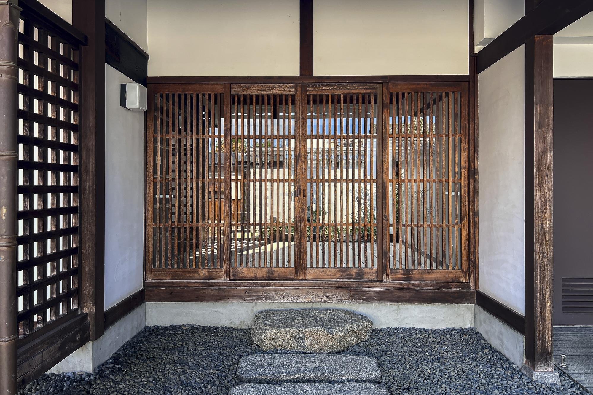 Traditional Japanese entrance with wooden lattice sliding door, gravel path, and stone steps.