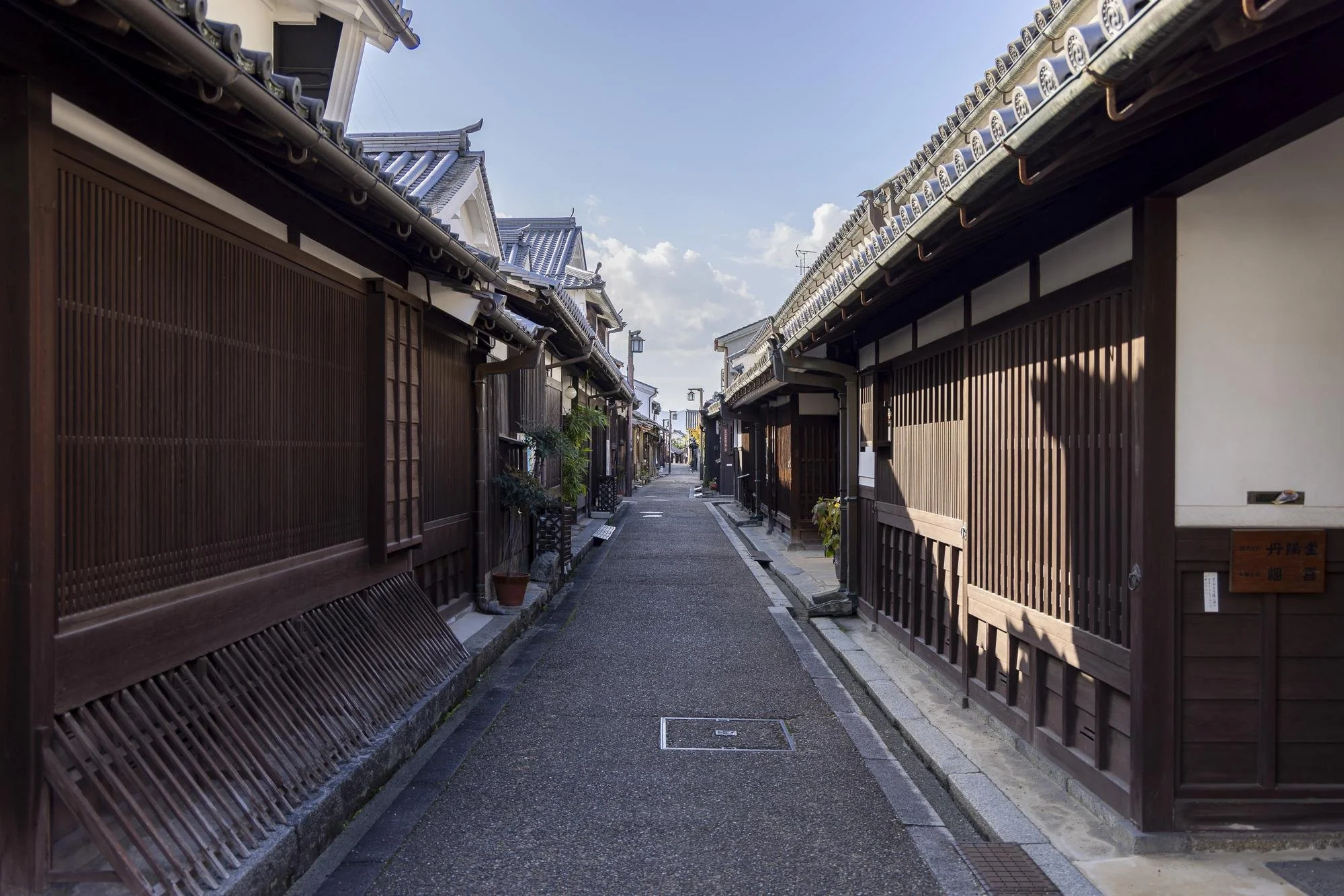A narrow alleyway with traditional Japanese wooden buildings on either side, with a clear blue sky above.