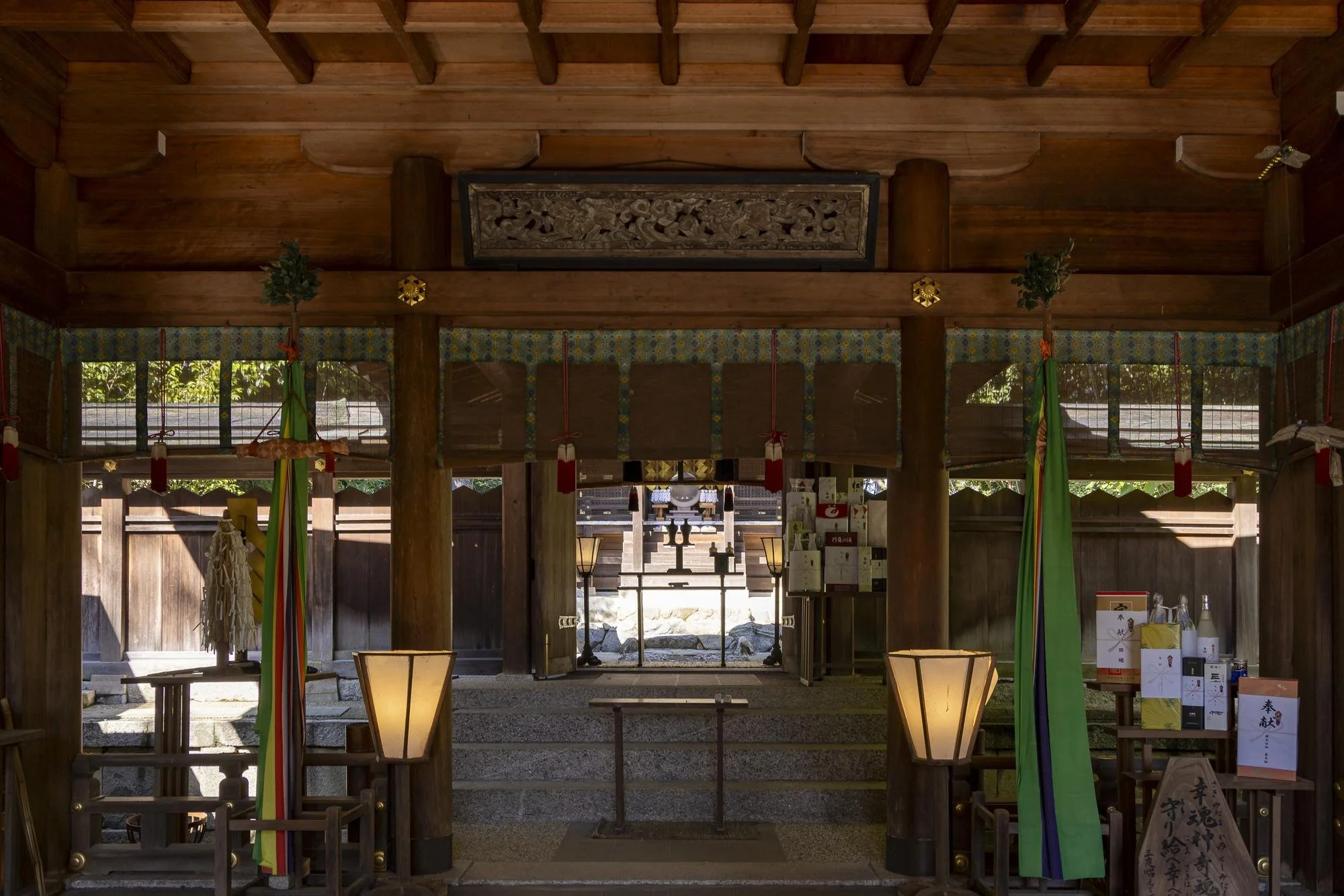 Interior view of a traditional Japanese shrine with wooden beams, lanterns, and offerings.