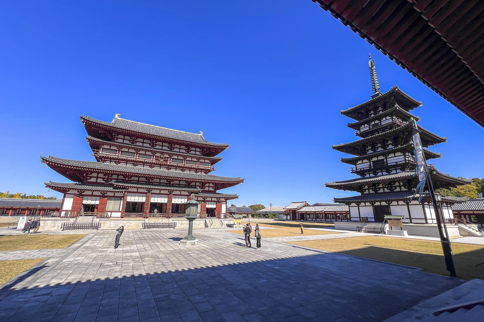 Traditional Japanese temple complex with a large main hall and a five-story pagoda, under a clear blue sky.