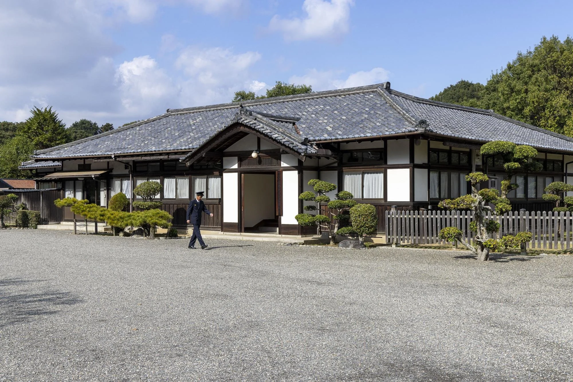 Traditional Japanese house with a gravel yard, manicured bushes, and a man in a suit walking