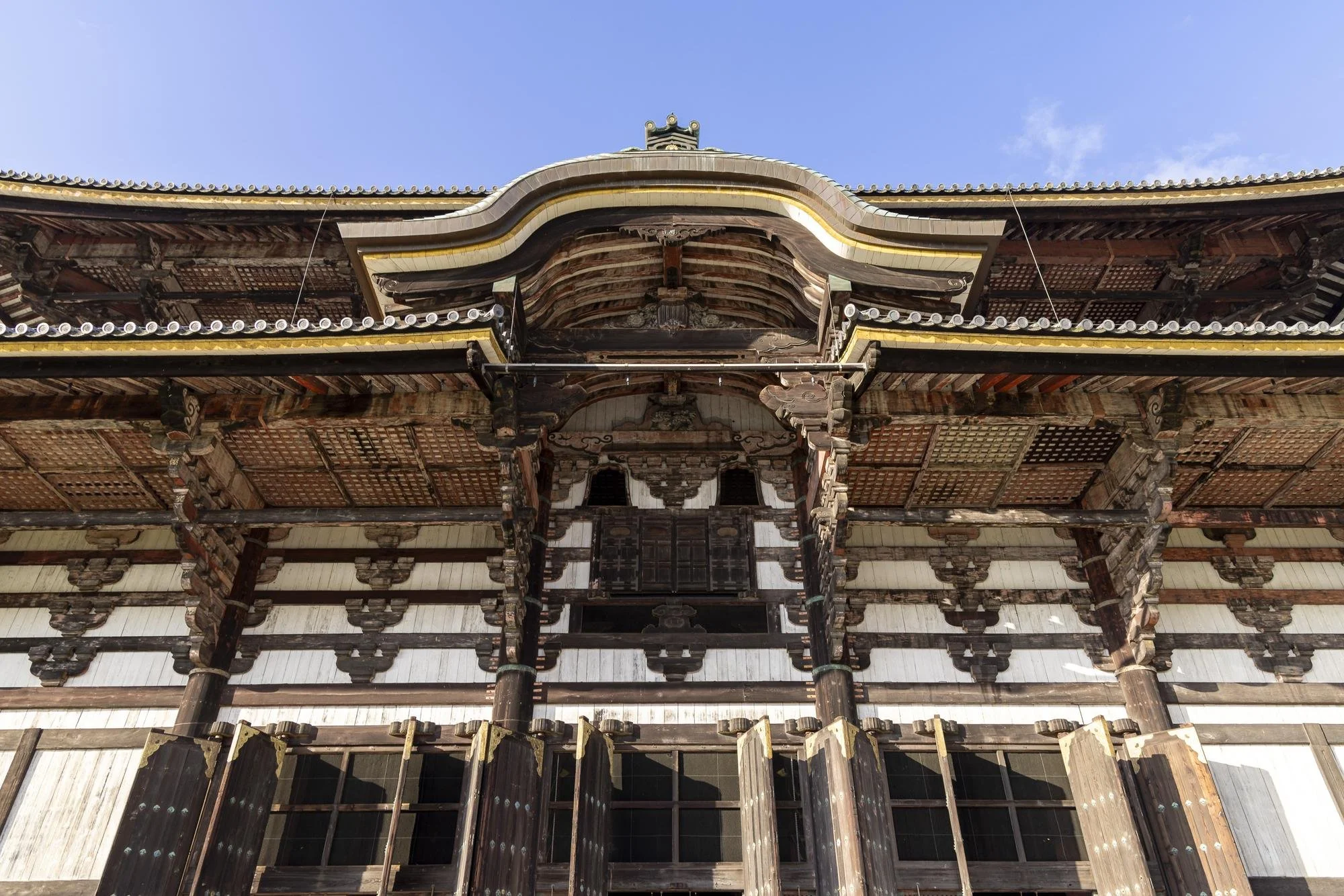 Front view of a traditional Japanese wooden temple building with intricate architectural details, under a clear blue sky.