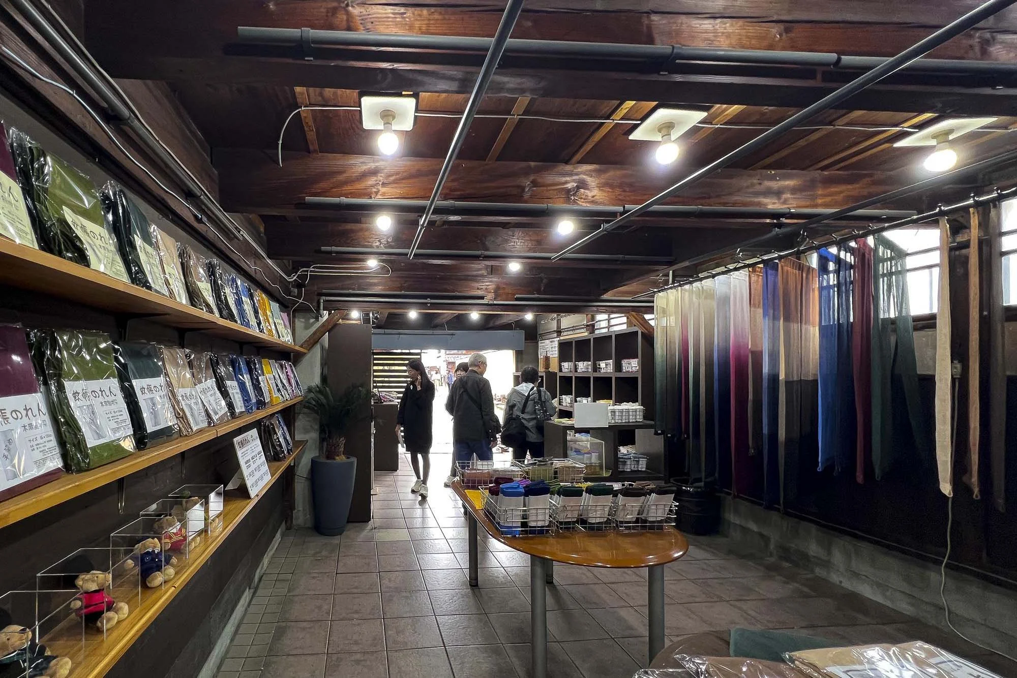 Indoor shop with shelves of fabric on the left, colorful fabric rolls on the right, and people browsing in the background.
