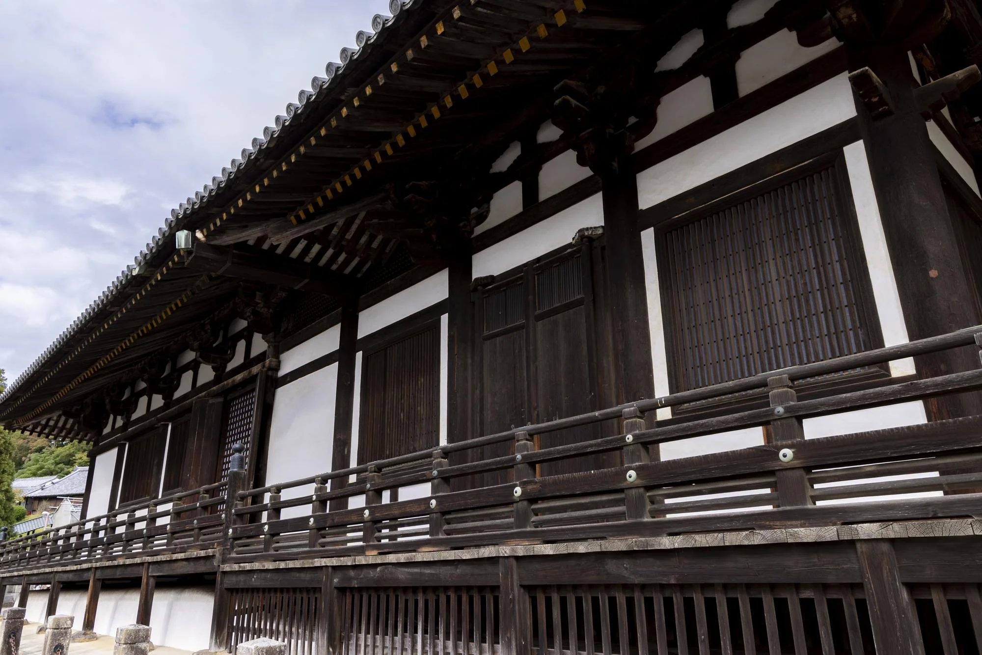 Traditional Japanese temple building with wooden structure, sliding doors, and tiled roof, set against a partly cloudy sky.