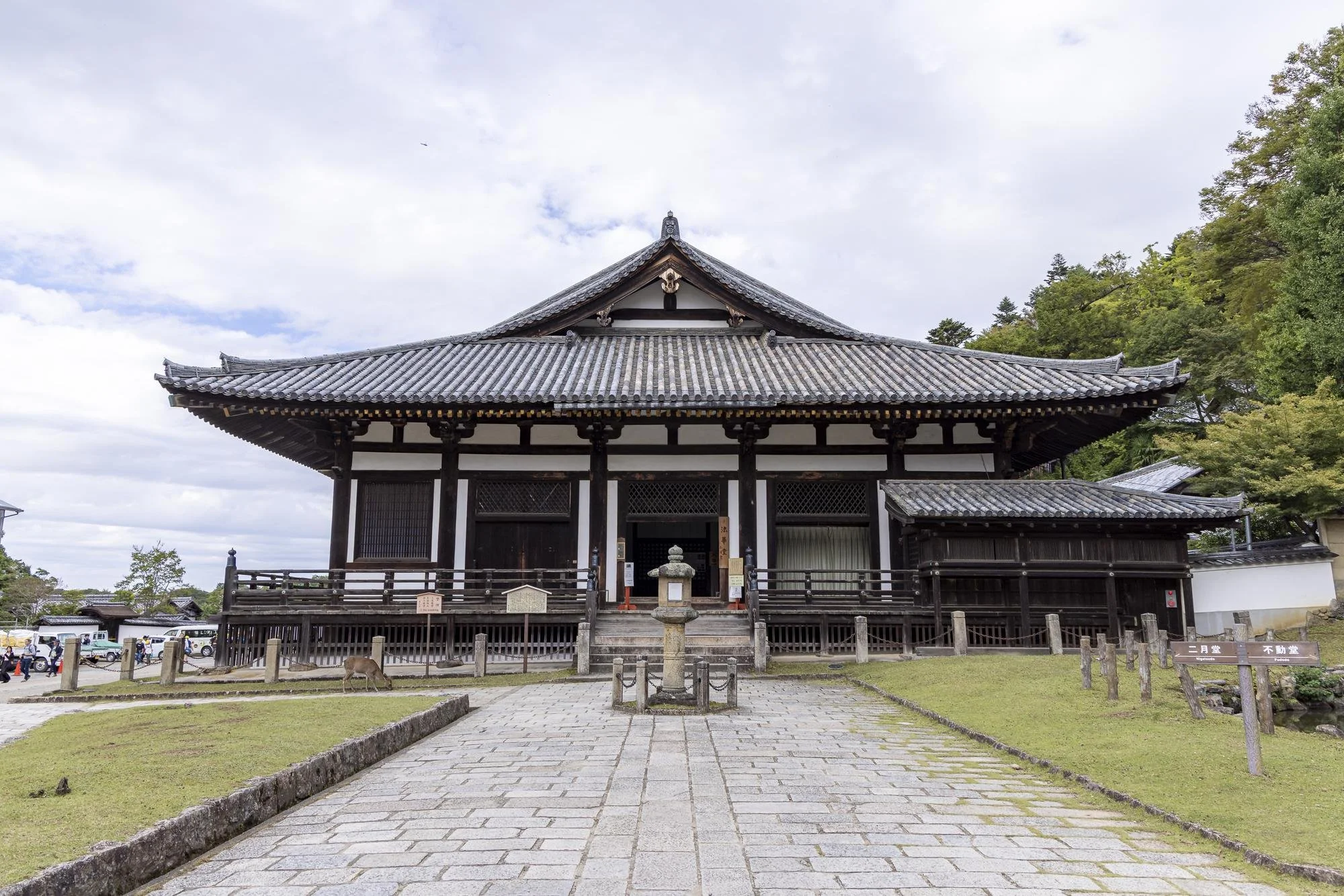 Sangatsu-do (Hokke-do): A traditional Japanese wooden temple with a tiled roof, steps leading up to the entrance, surrounded by a paved pathway and green grass, with trees in the background.