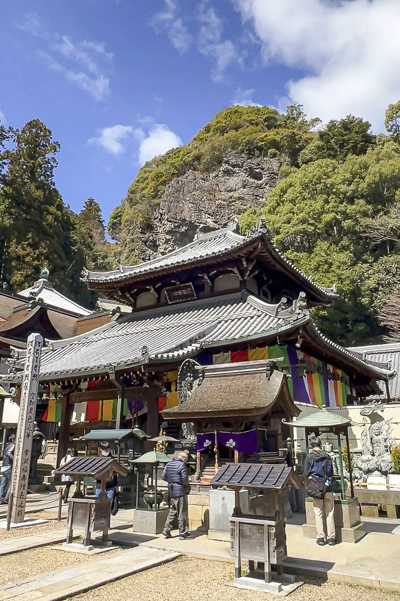 Traditional Japanese temple with people praying, colorful banners, and a mountain in the background.