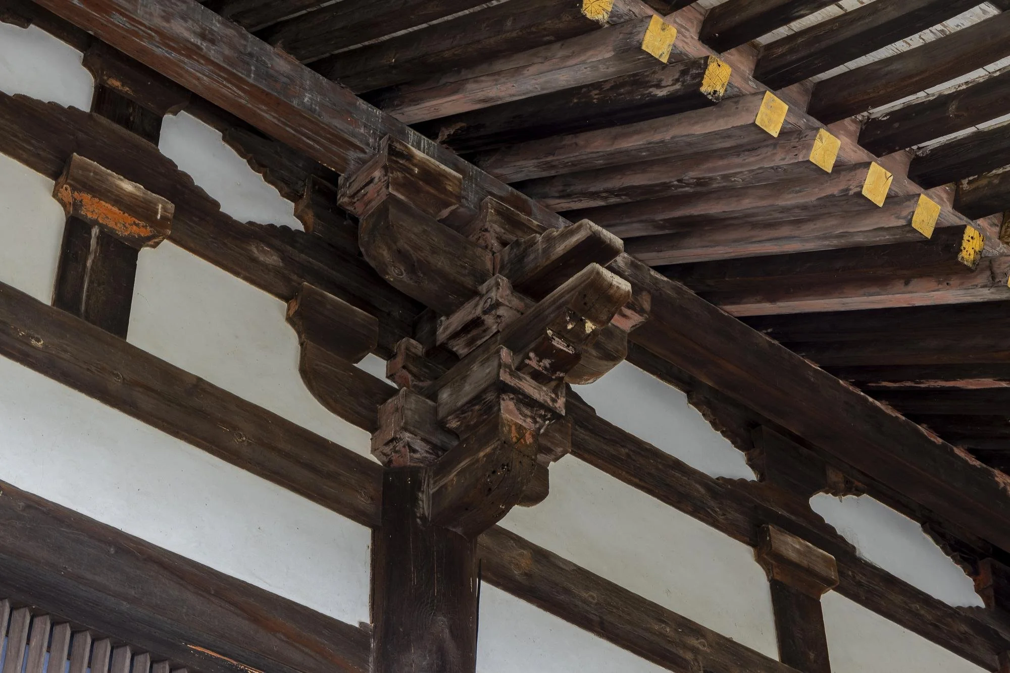 Close-up of traditional wooden architectural beams and supports in a historical building, showing dark stained wood with some yellow accents.