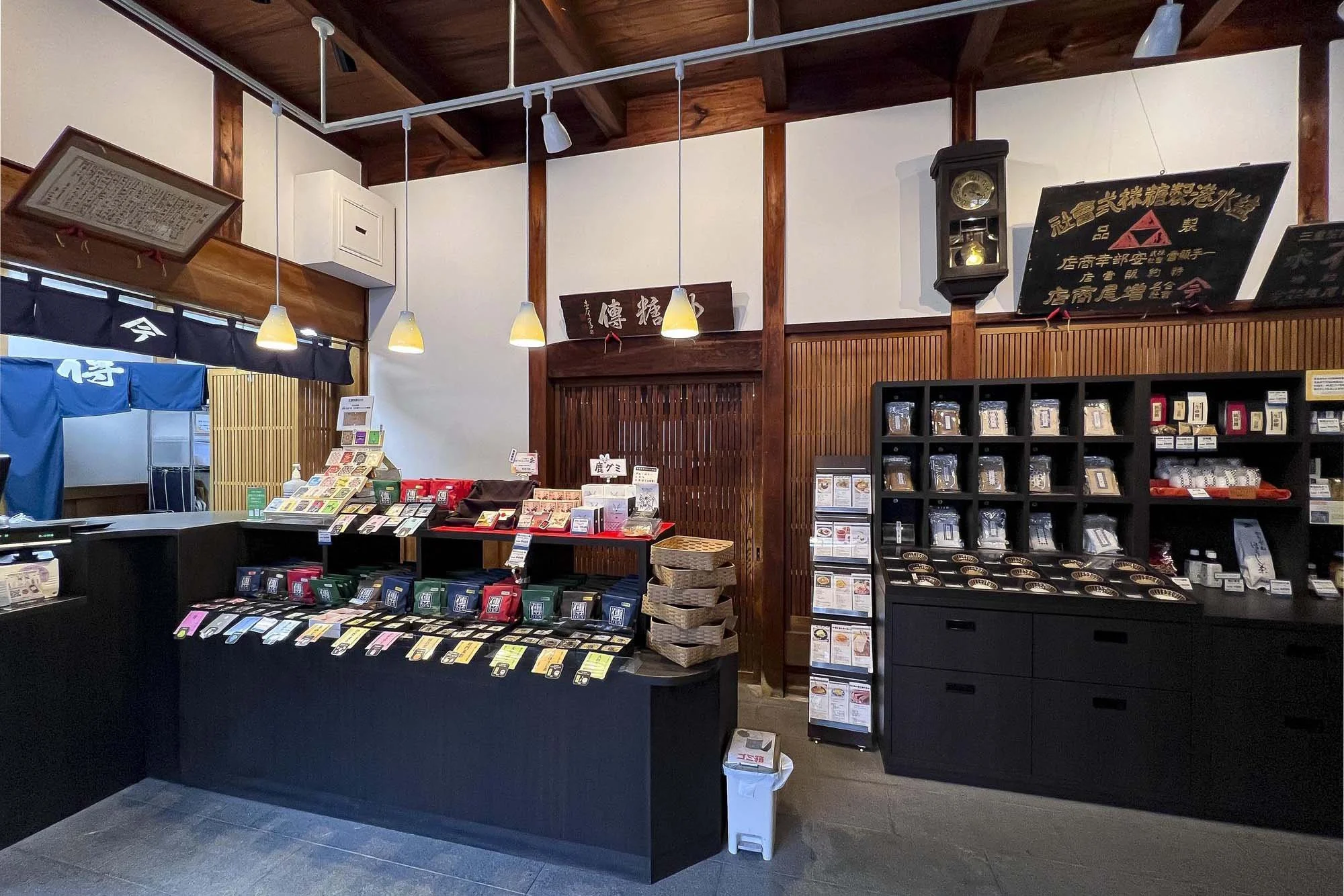 Interior of a Japanese store with wooden decor, displaying various packaged food products and tea on black shelves and counters.