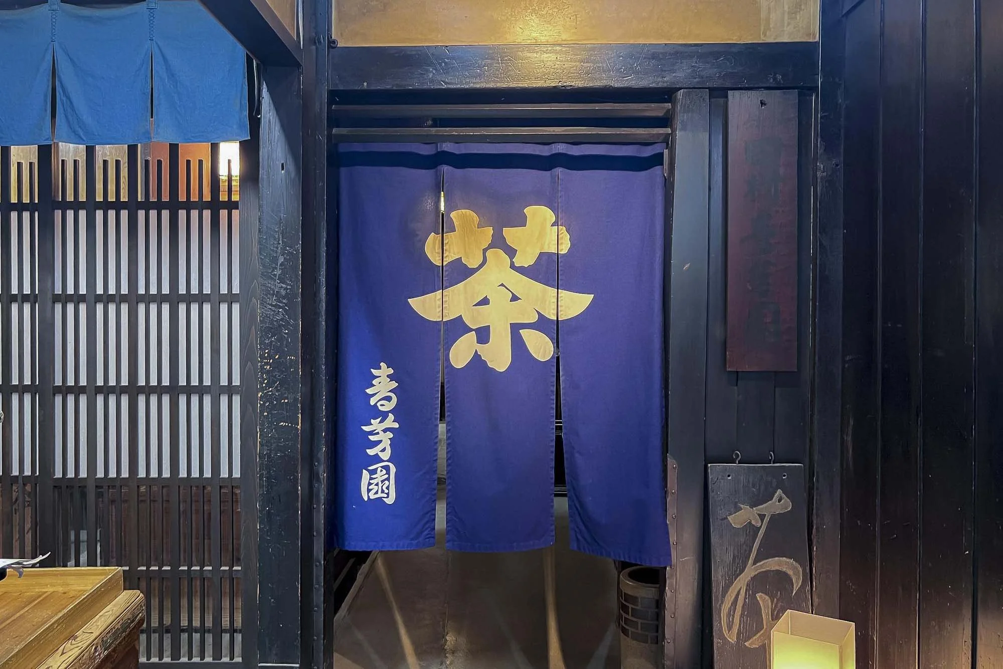 Entrance to a Japanese restaurant with a dark blue noren curtain featuring a yellow symbol, and white Japanese characters on the left side.