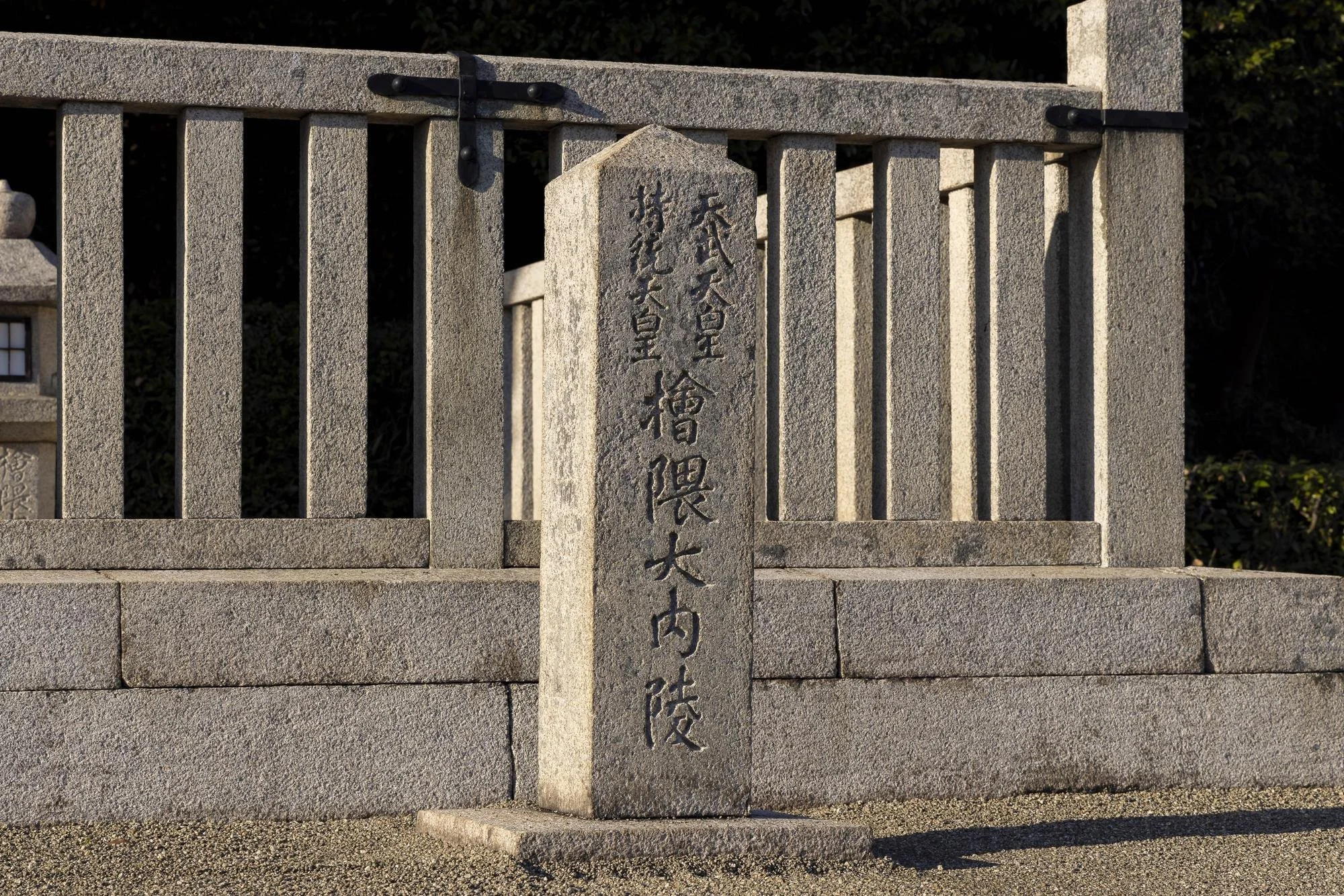 Stone monument with Japanese inscriptions in front of a concrete fence.