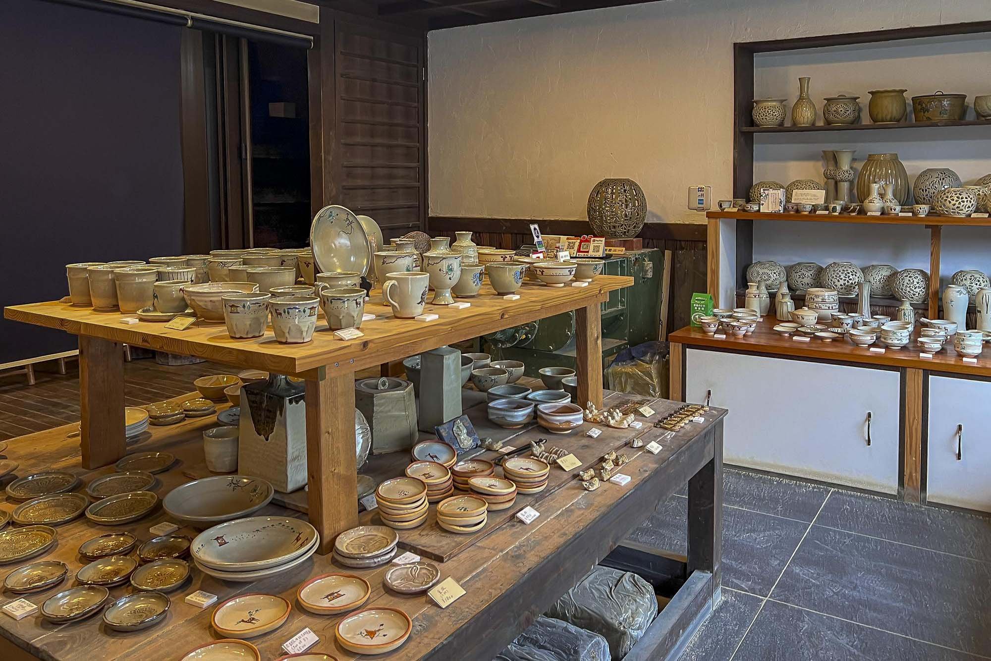 Display of various pottery and ceramic items in a shop, including bowls, mugs, and vases arranged on wooden shelves and tables.