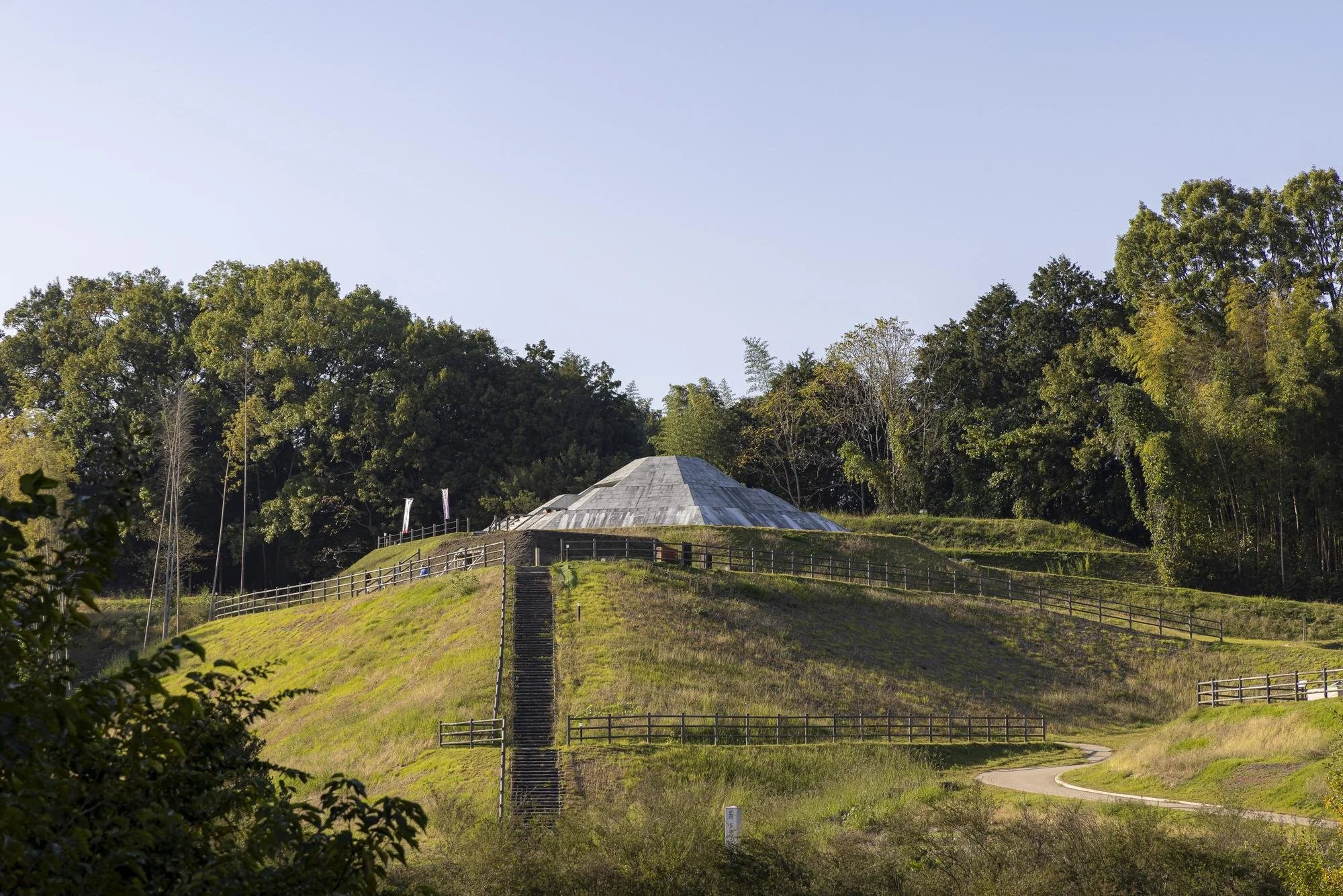 A hill with a winding path, fenced stairs, and a domed structure at the top, surrounded by trees under a clear blue sky.