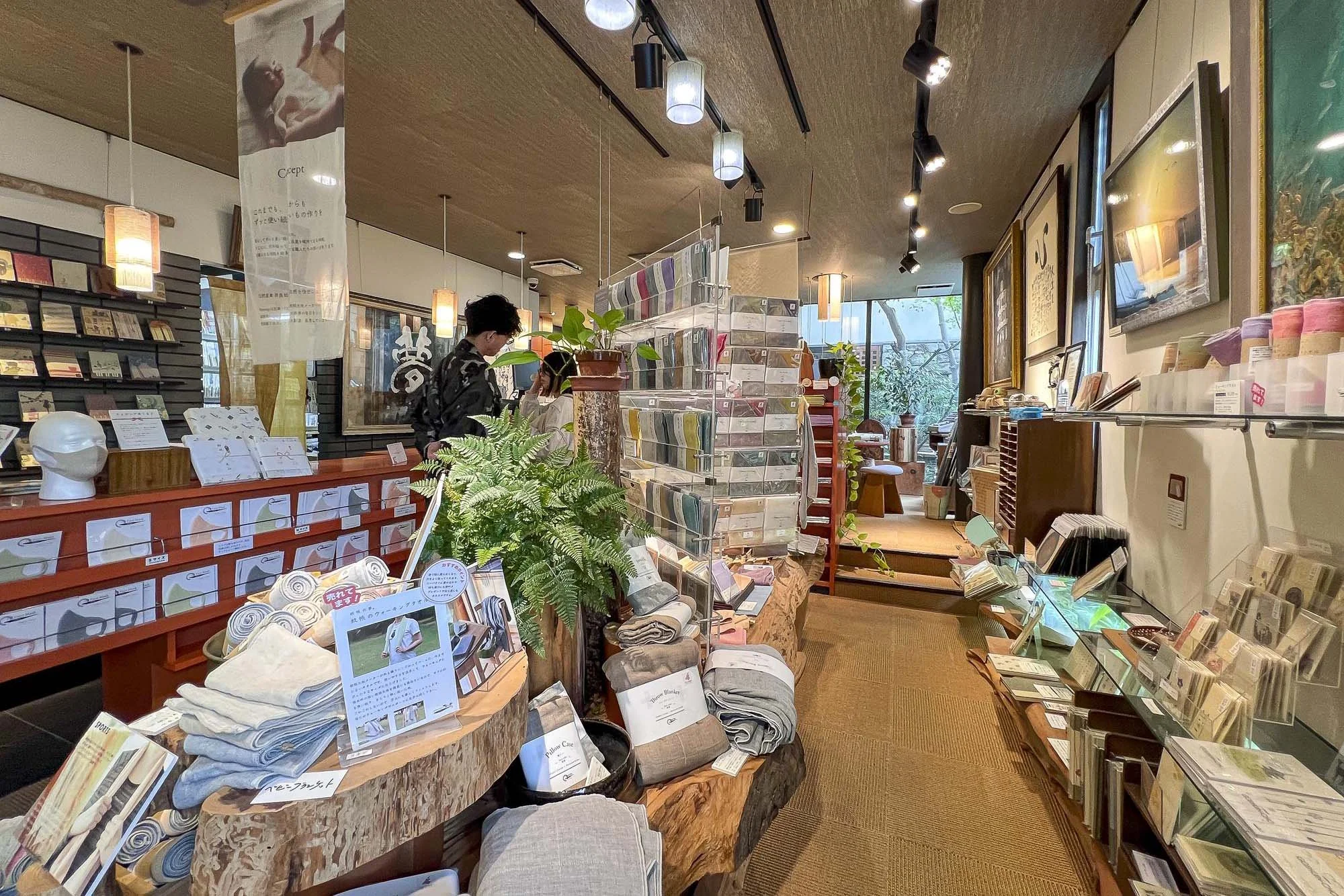 Interior of a store with shelves of colorful fabrics, towels, and books, and customers browsing.