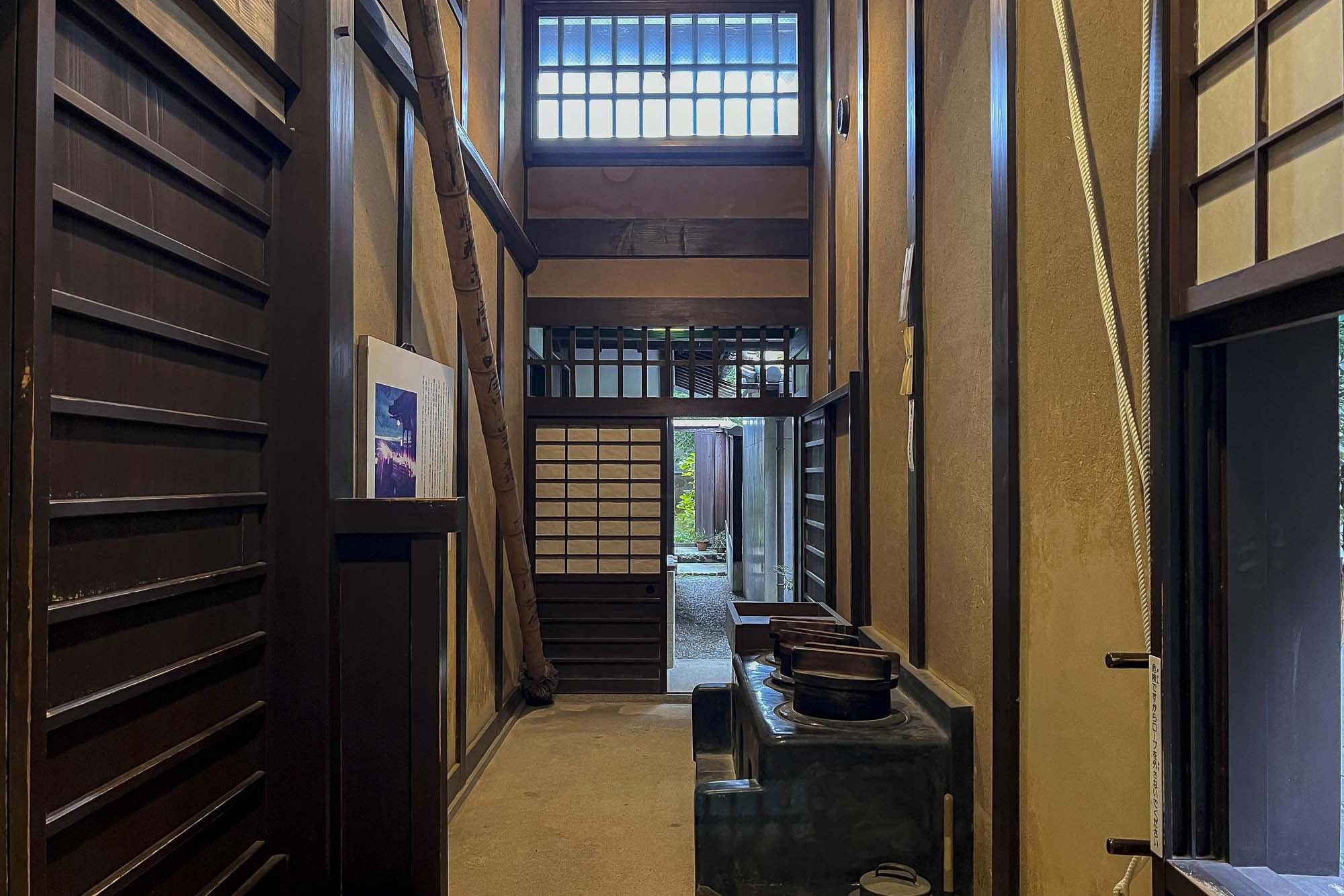 Traditional Japanese-style hallway with wooden wall panels, shoji screens, and a small entrance visible at the end.