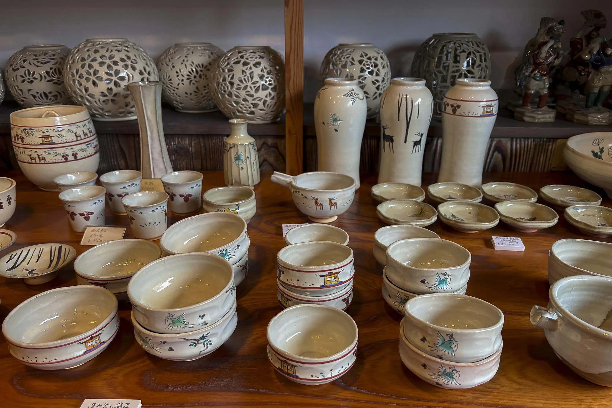 Collection of ceramic bowls and vases with traditional Asian designs, displayed on a wooden table with decorative openings on some vases and bowls for floral or geometric patterns.
