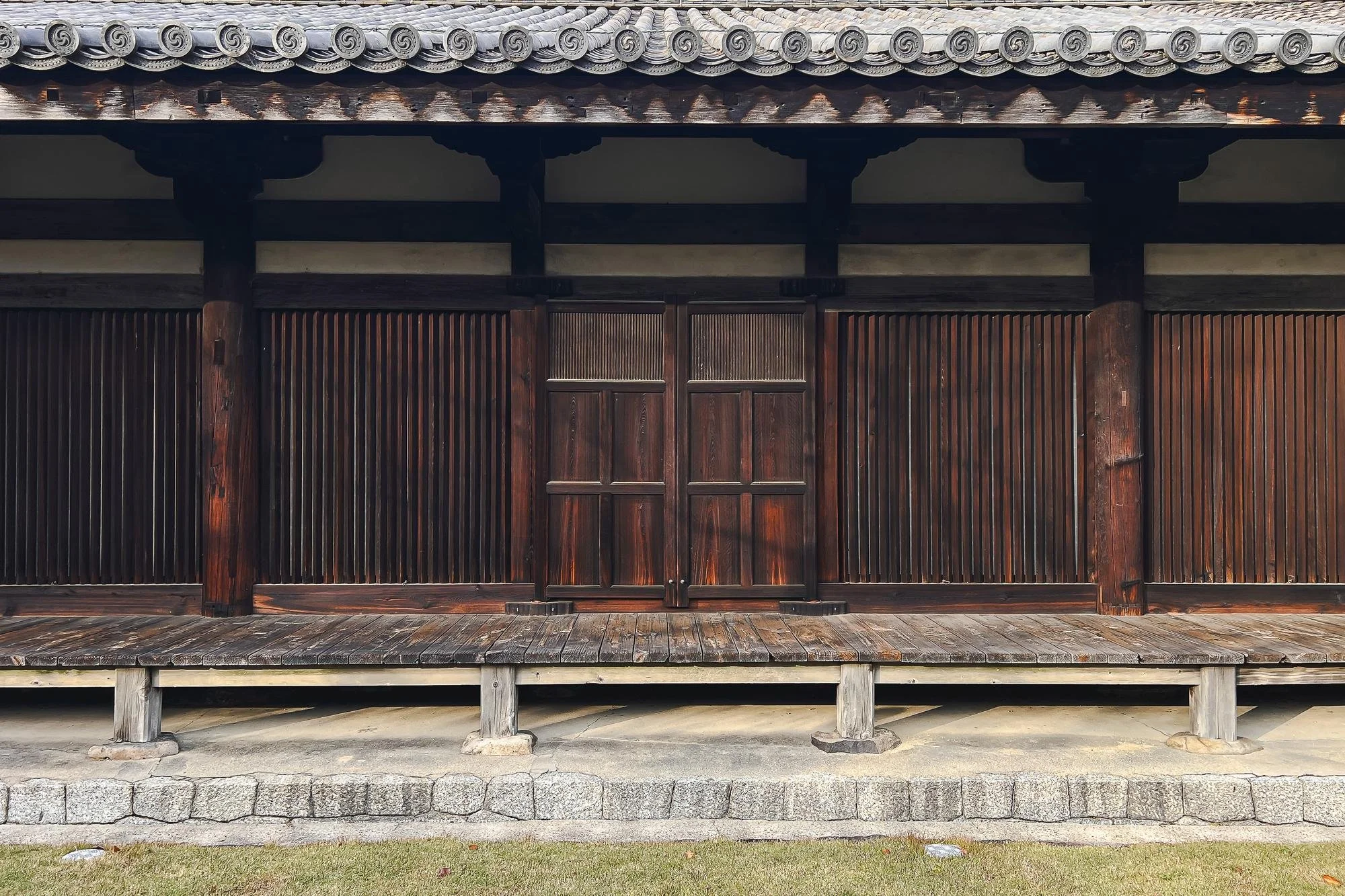 A traditional Japanese wooden building with sliding doors, a tiled roof, and a platform with wooden steps.