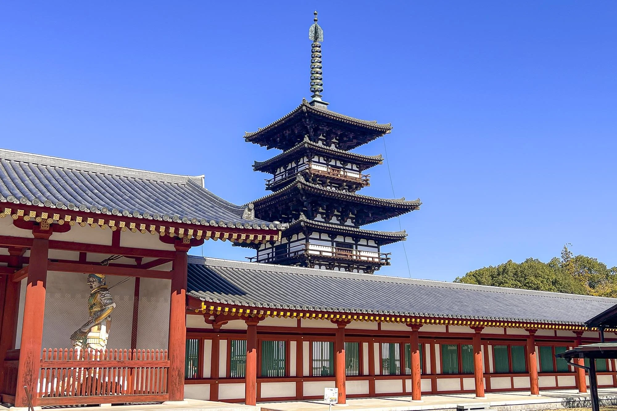 Traditional Japanese temple with a pagoda tower, red and white structures, surrounded by a blue sky with clouds.
