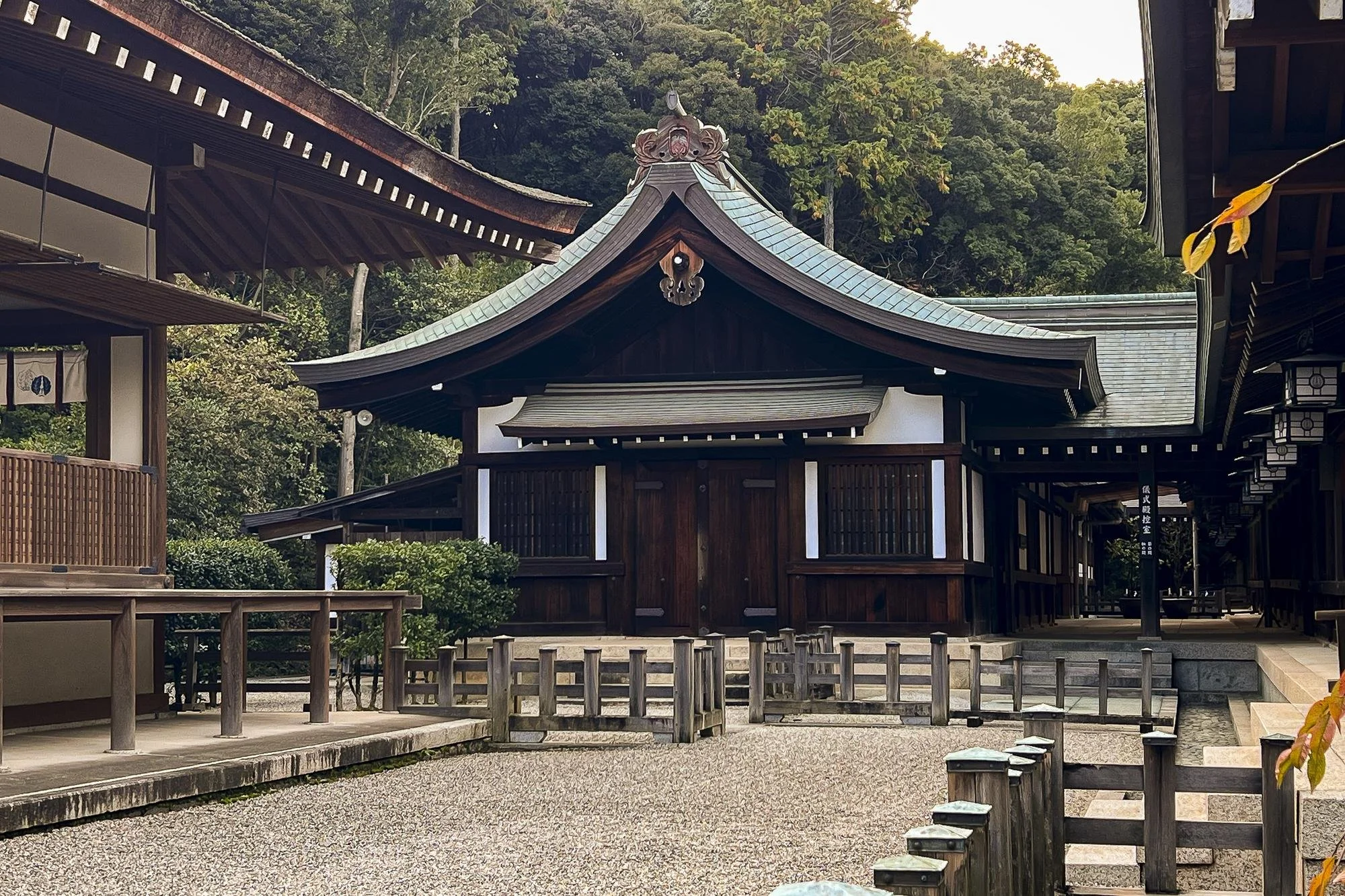 Traditional Japanese shrine with wooden structures and a tiled roof, surrounded by trees.
