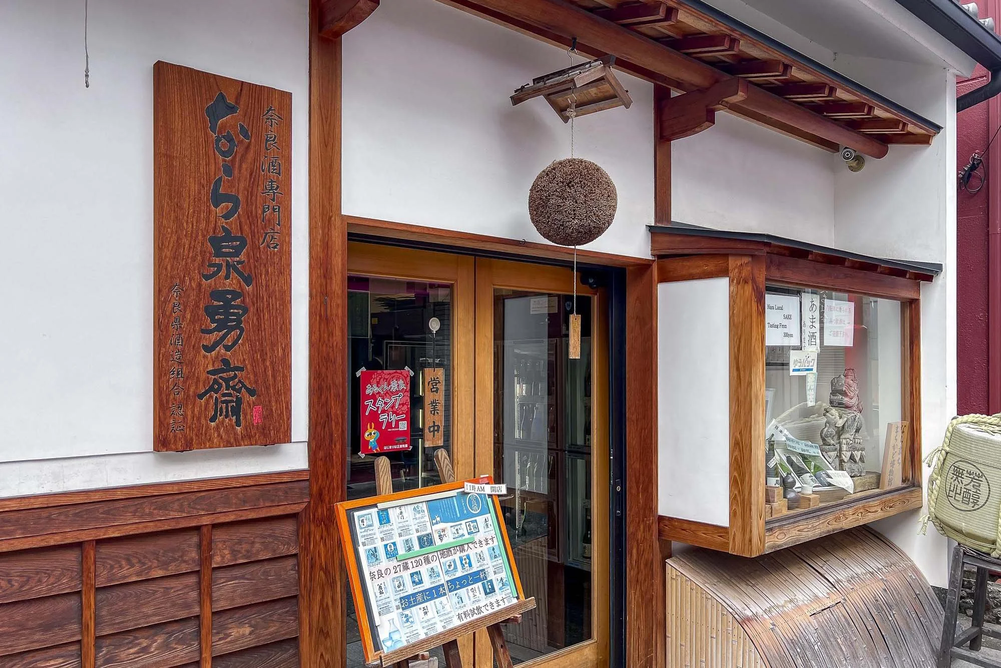 The exterior of a Japanese restaurant with wooden accents, a hanging round decoration, and a display window showing sculptures and signs.