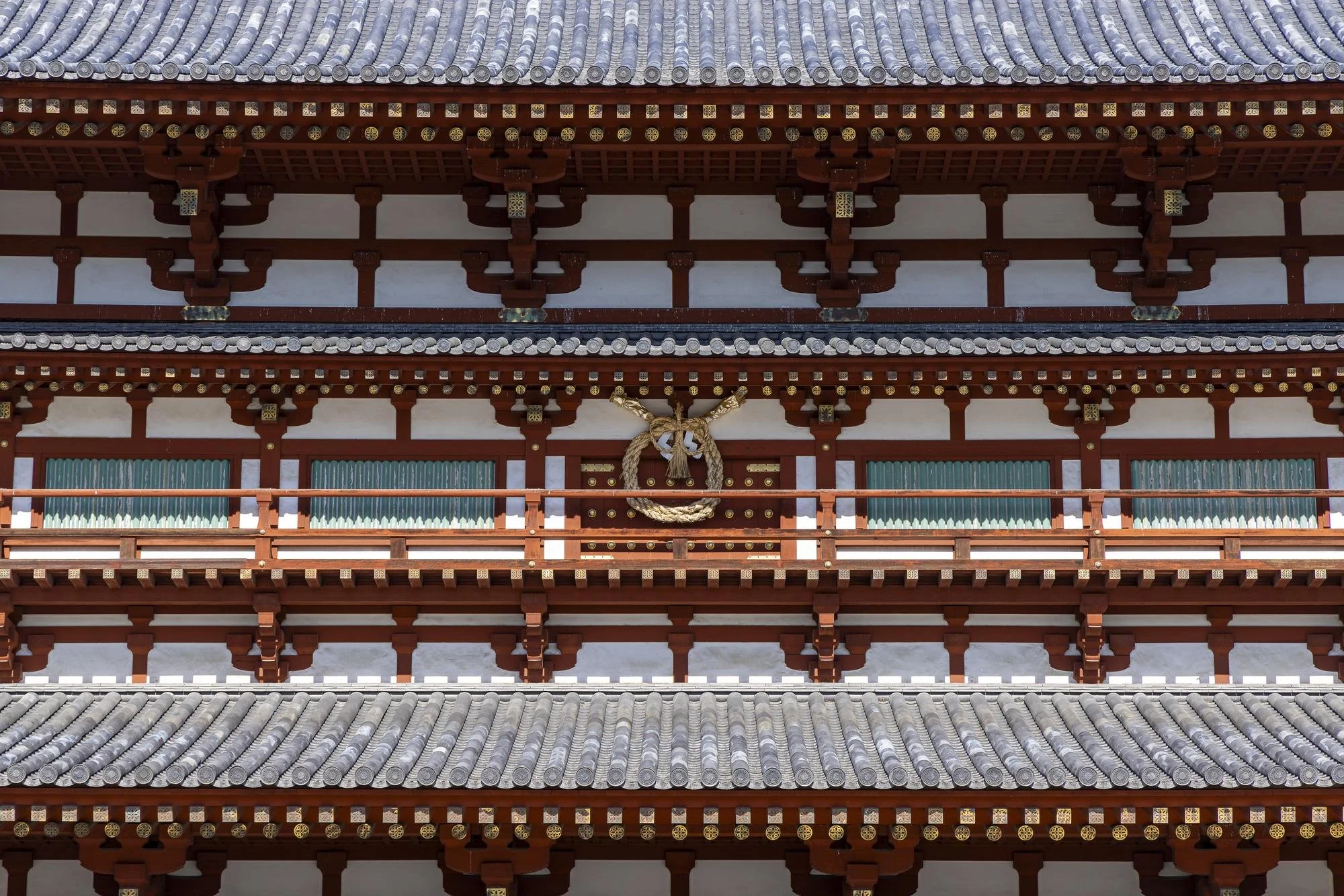 Close-up of traditional Japanese temple roof with layered eaves, decorative woodwork, and a shimenawa (sacred rope) hanging on the wooden structure.