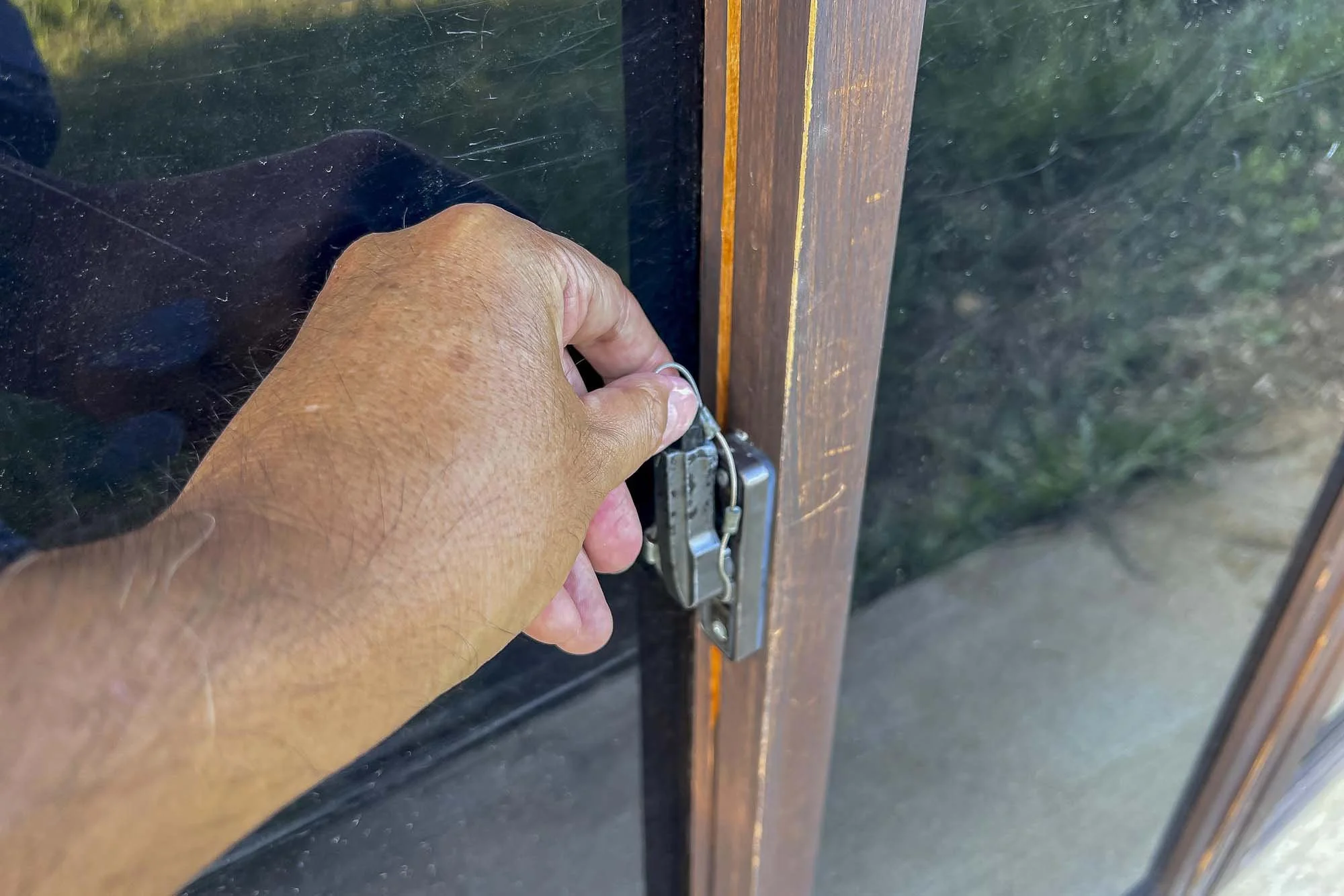A hand locking a door with a metal padlock on a glass door with a wooden frame.