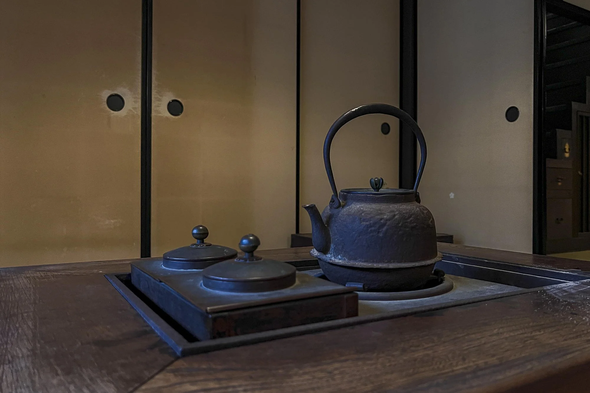 Old black iron kettle on a wooden table in a traditional Japanese room with sliding paper doors.